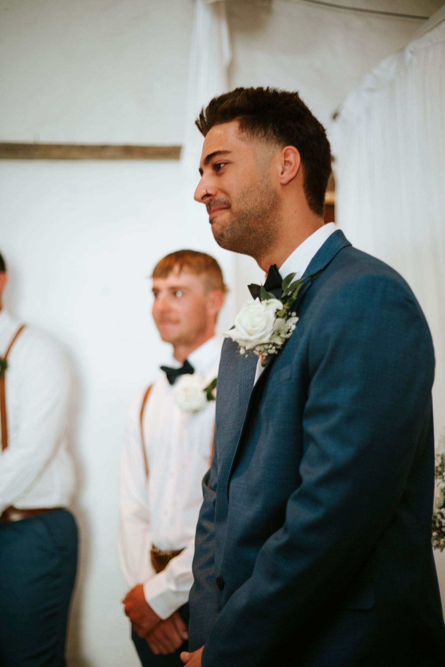 Groom in blue suit smiling at wedding ceremony with groomsmen standing behind him.
