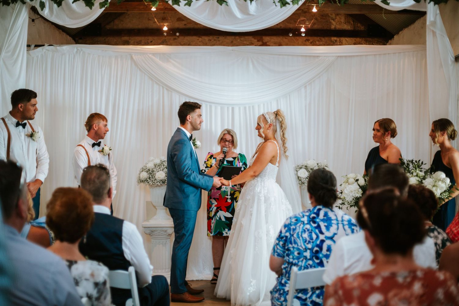 Bride and groom exchange vows at decorated altar surrounded by wedding guests.