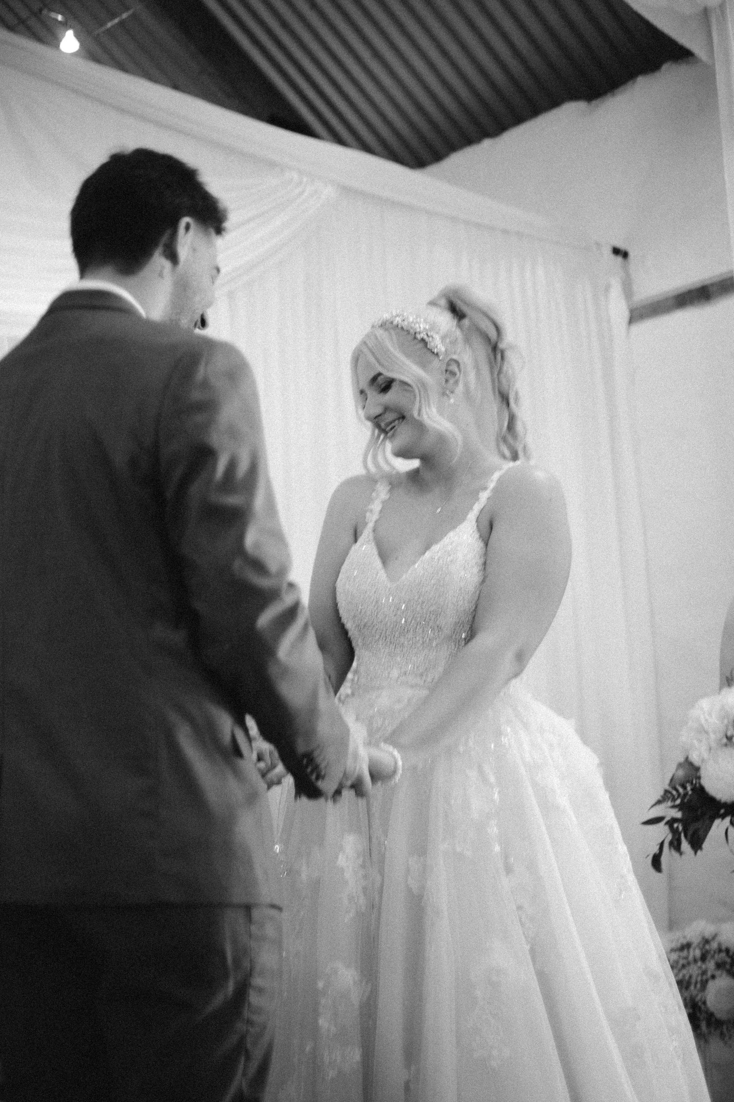 Black and white photo of bride and groom holding hands during wedding ceremony.