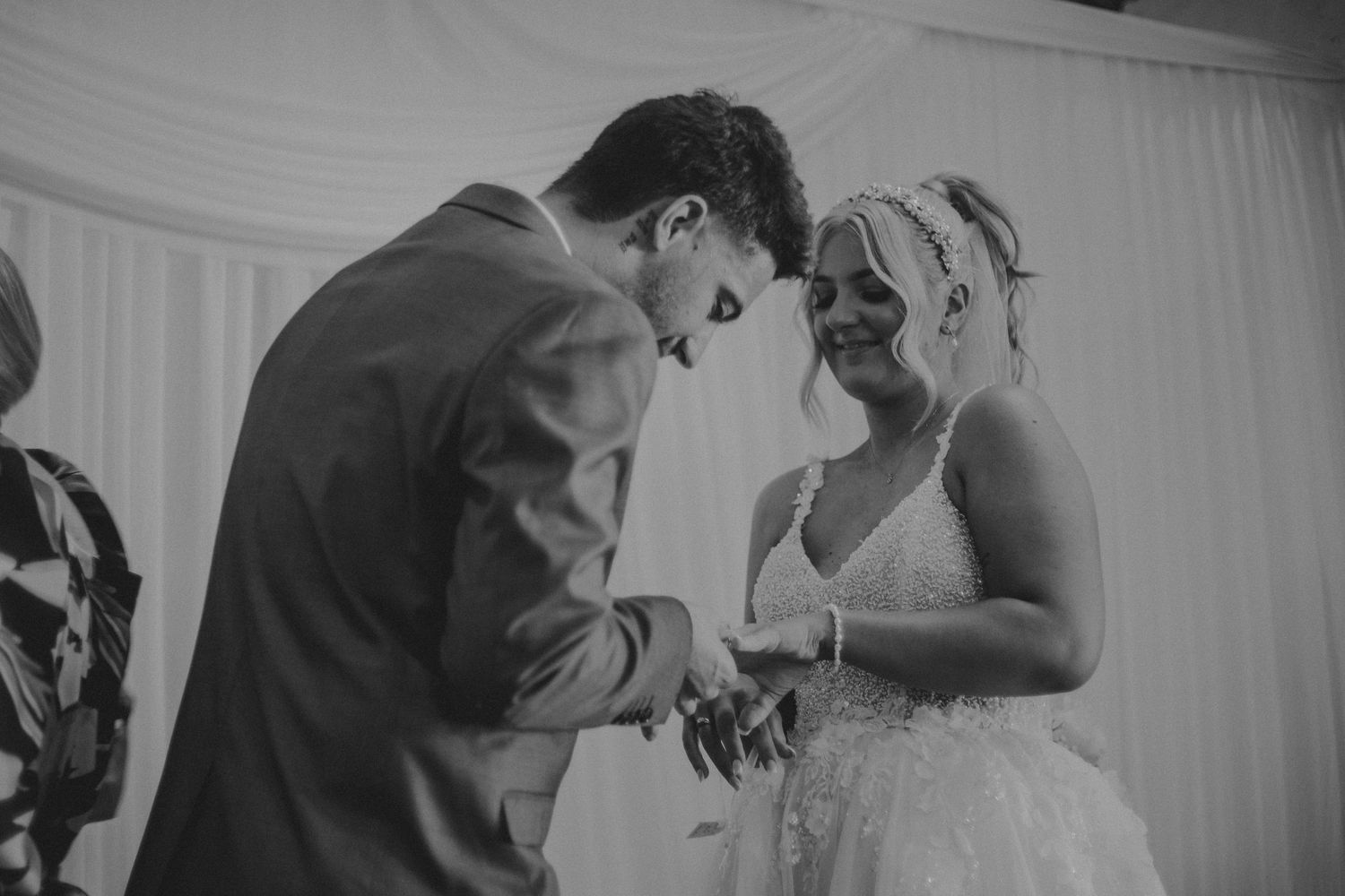 Black and white photo of groom placing wedding ring on brides finger at altar.