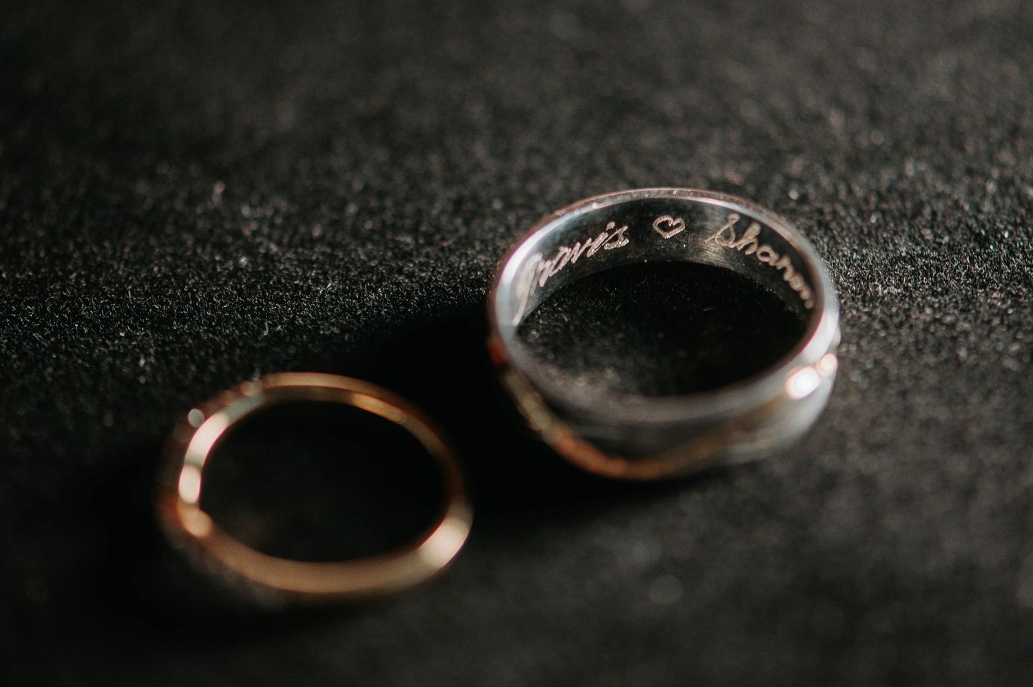 Two wedding rings, one gold and one silver, photographed on a dark textured surface.
