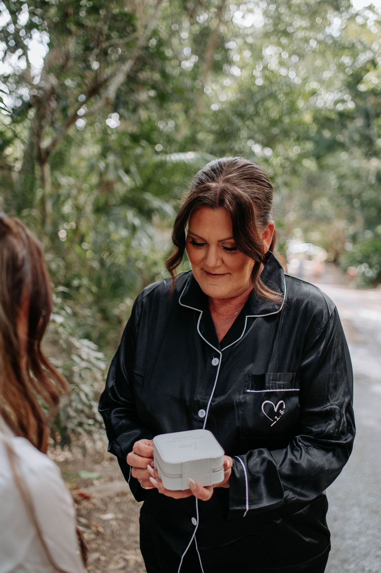 Someone wearing a black satin robe holds a small gift box during wedding preparations.