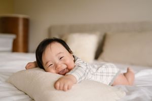A baby sleeping peacefully in white bedding with their tiny hand visible on the pillow.