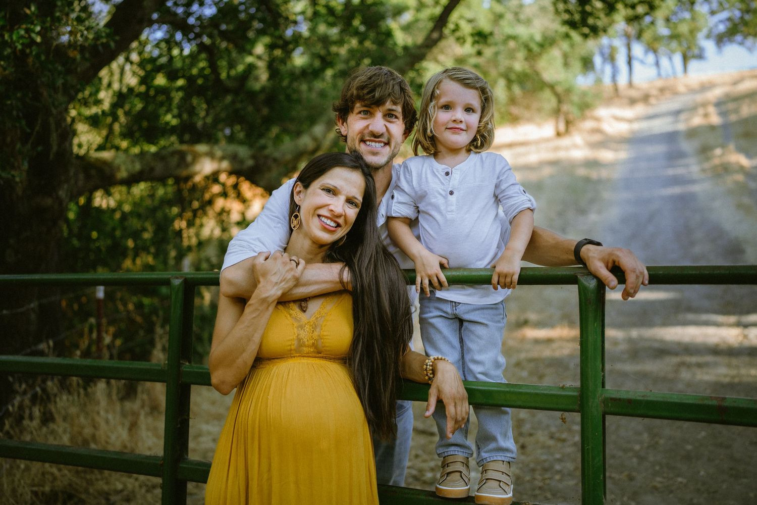 Family photoshoot beside a green fence in a park setting during late afternoon.
