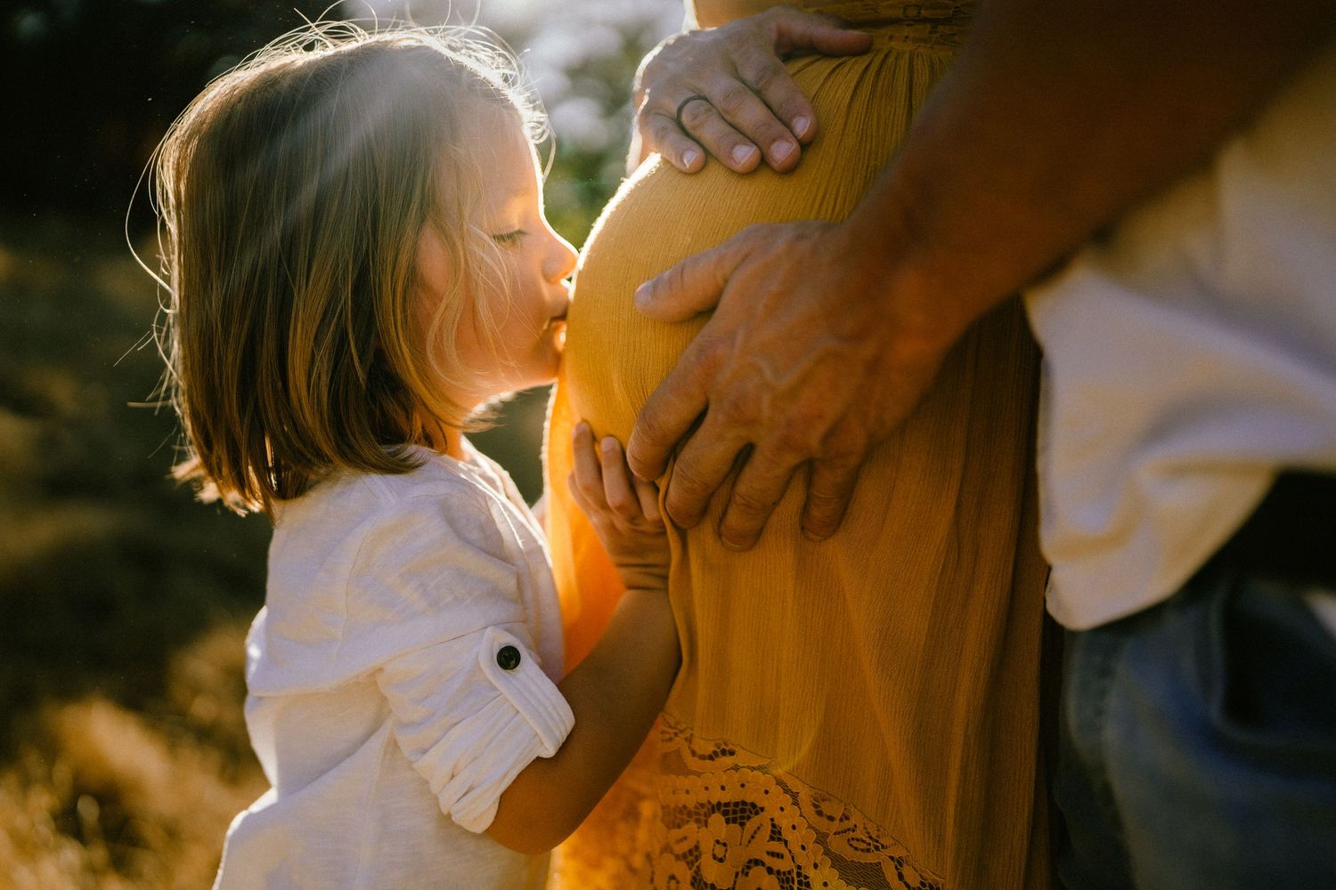 Intimate maternity photo session with golden sunlight filtering through trees.