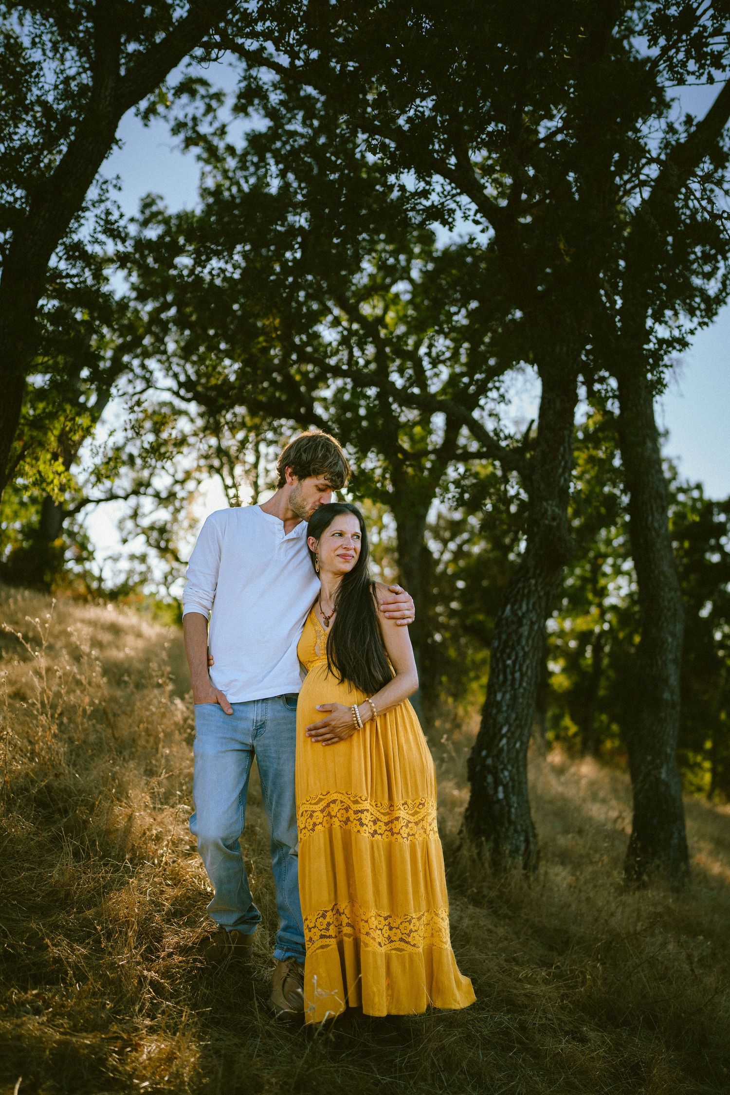 Artistic maternity portraits among oak trees with dappled sunlight and yellow dress.