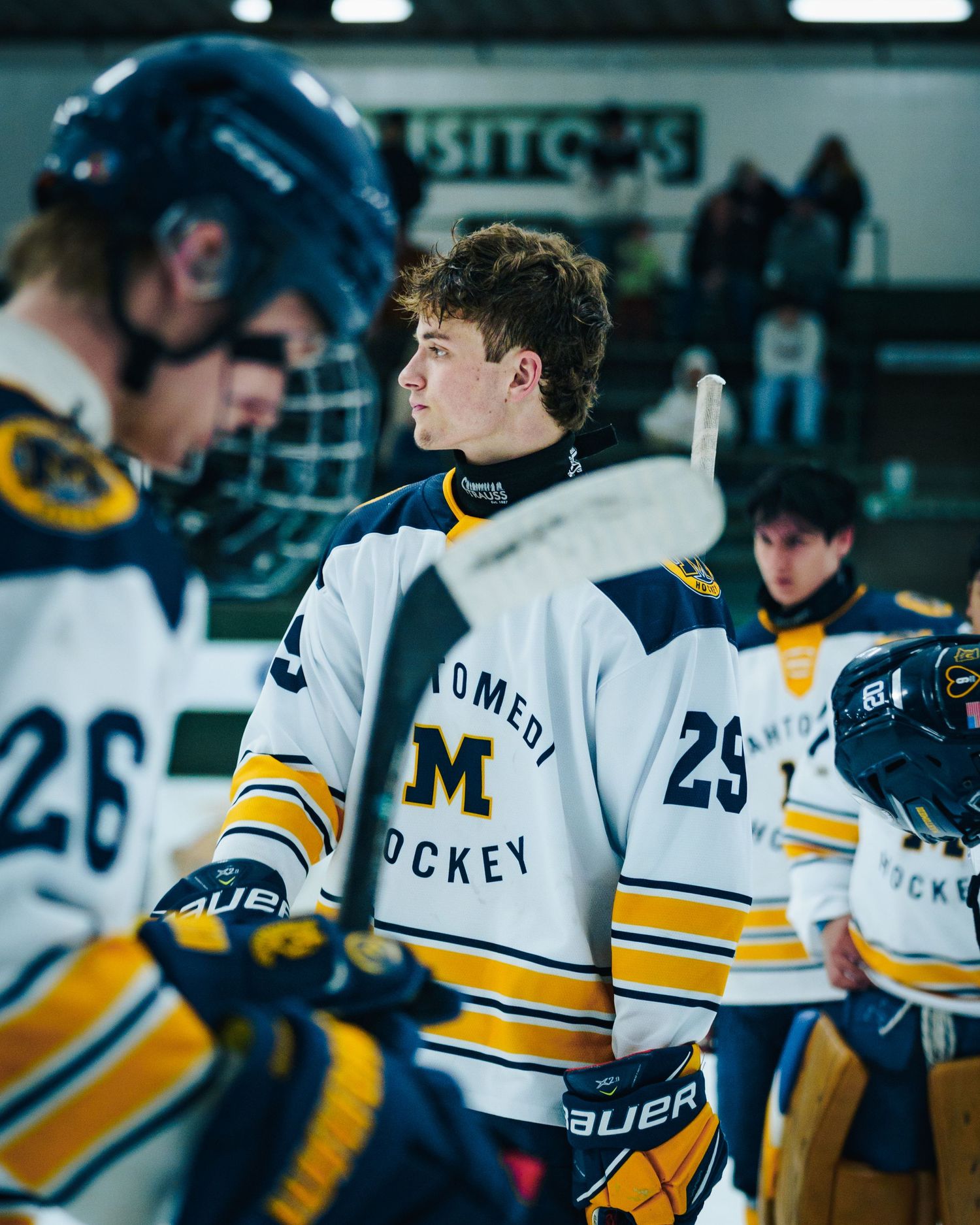 Hockey players in white and yellow jerseys line up on bench during game.