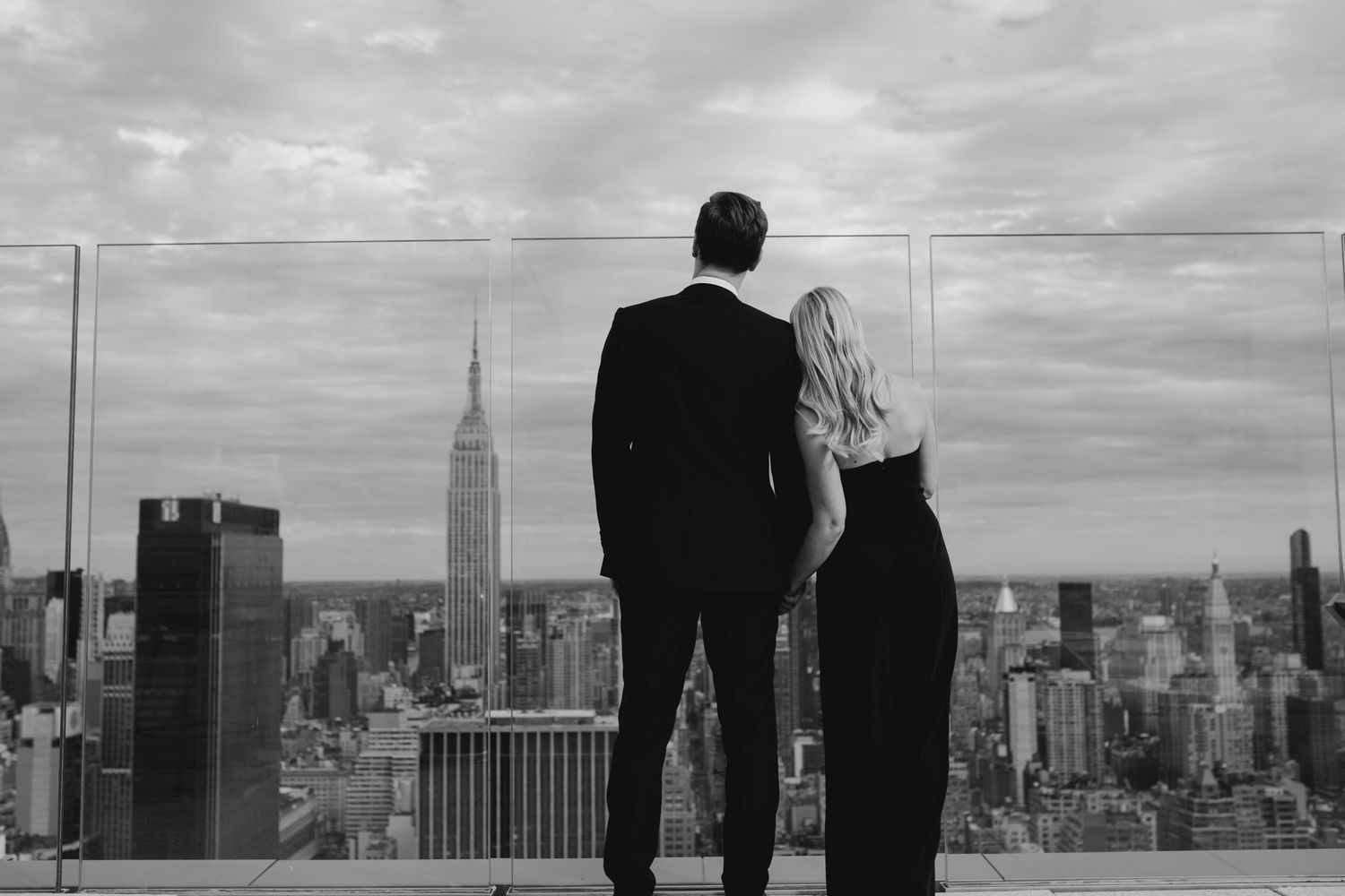 A couple admires the New York City skyline with the Empire State Building from an observation deck.