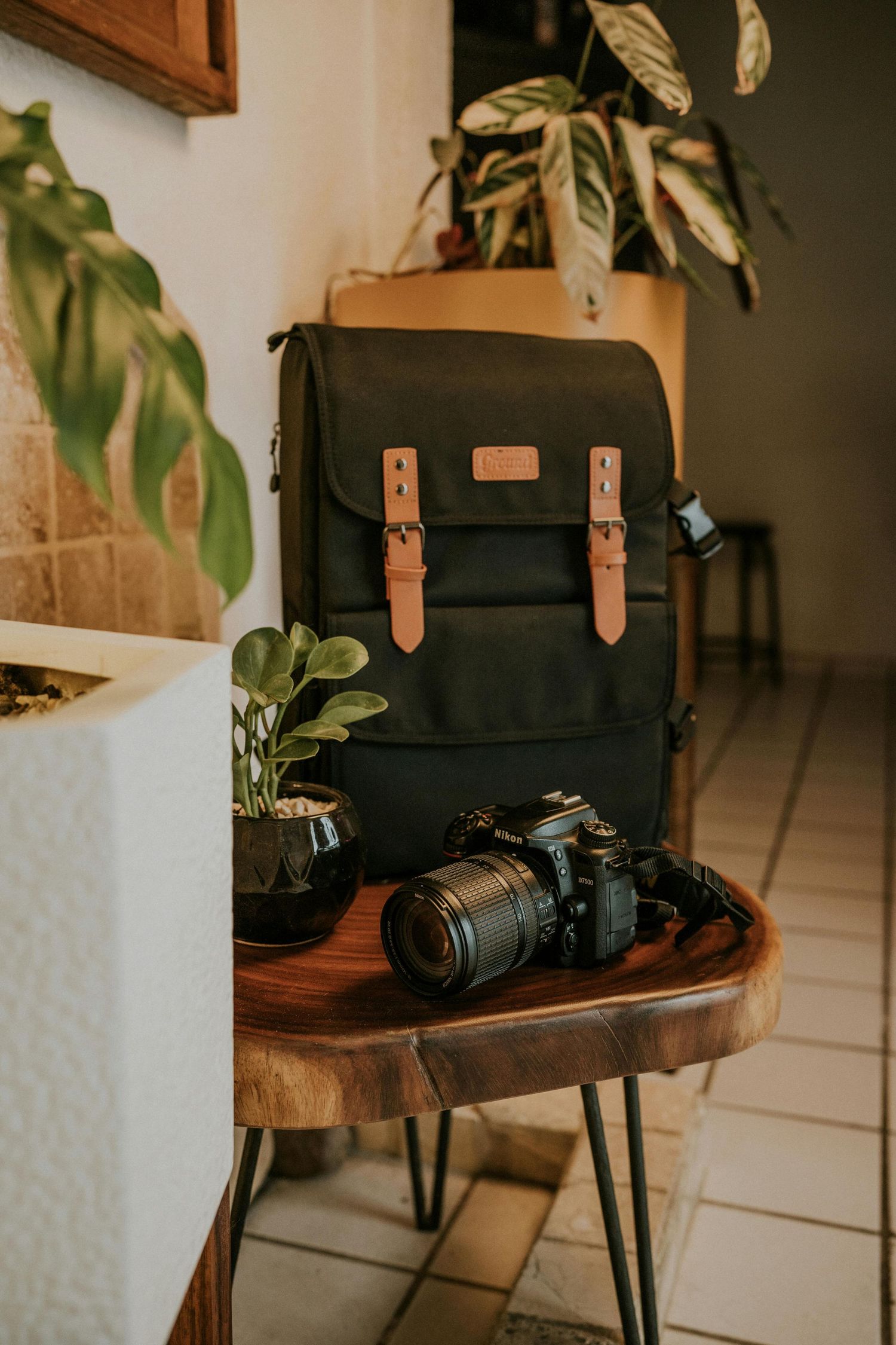 Black vintage camera bag and DSLR camera on wooden table with houseplants.