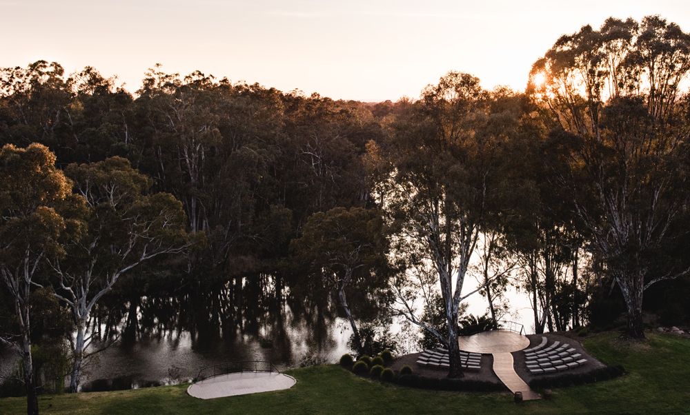 Panoramic sunset view of lakeside landscape with trees silhouetted against orange sky.