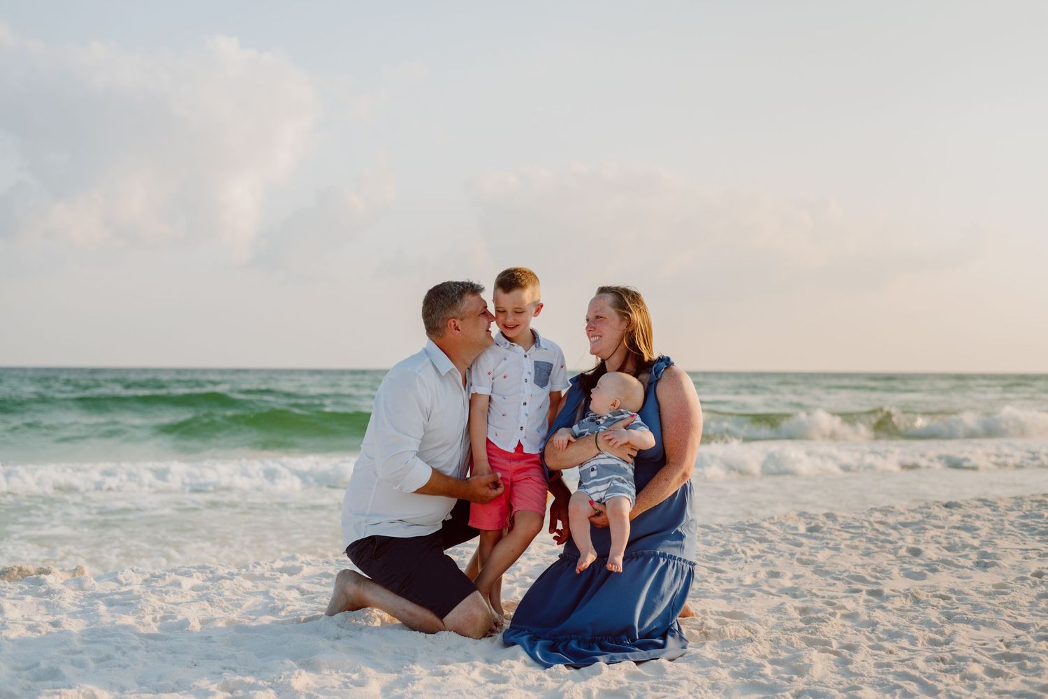 Family portrait on white sandy beach with turquoise ocean waves in background.