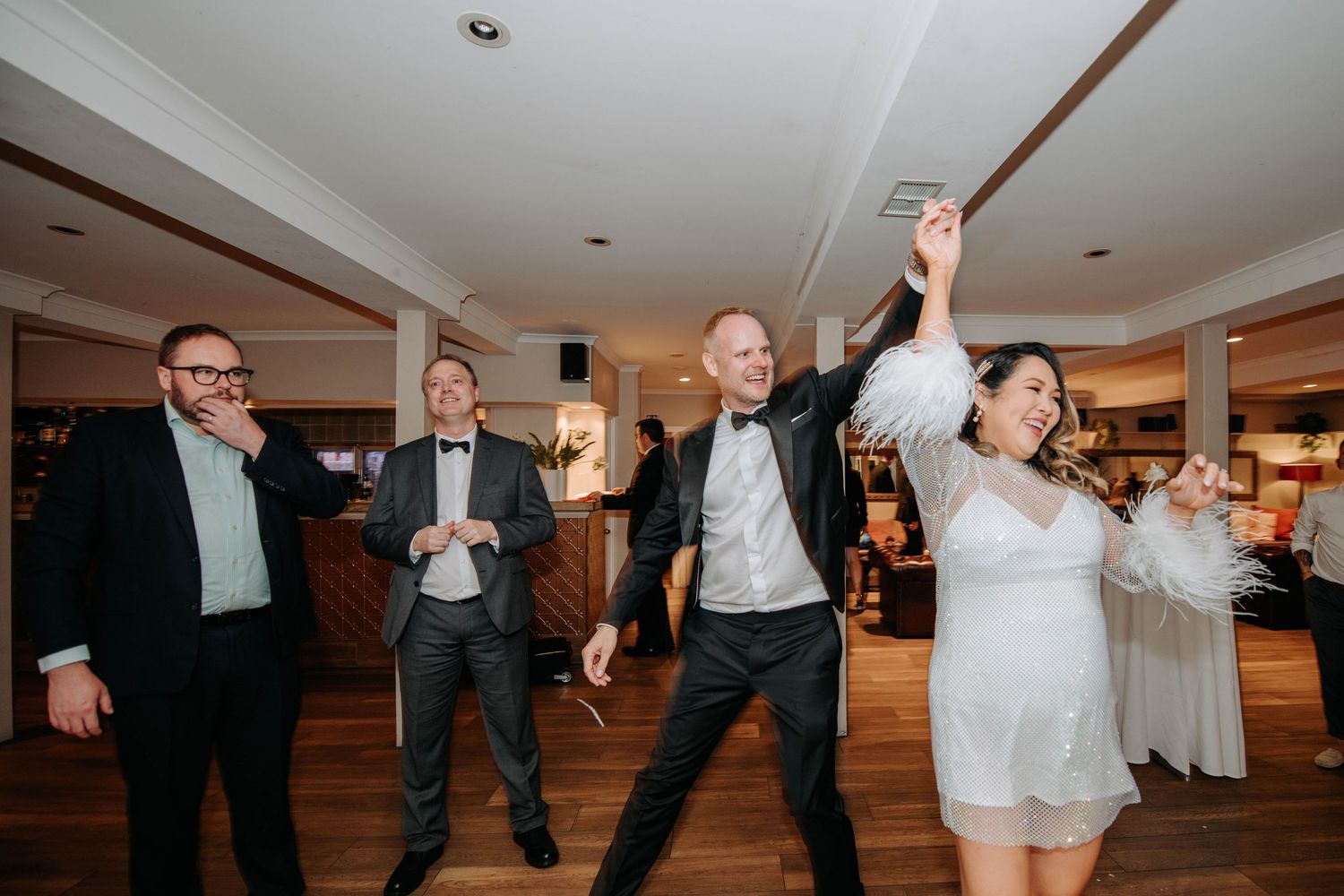 Celebrations and dancing at a wedding reception with guests in formal attire on a hardwood floor.