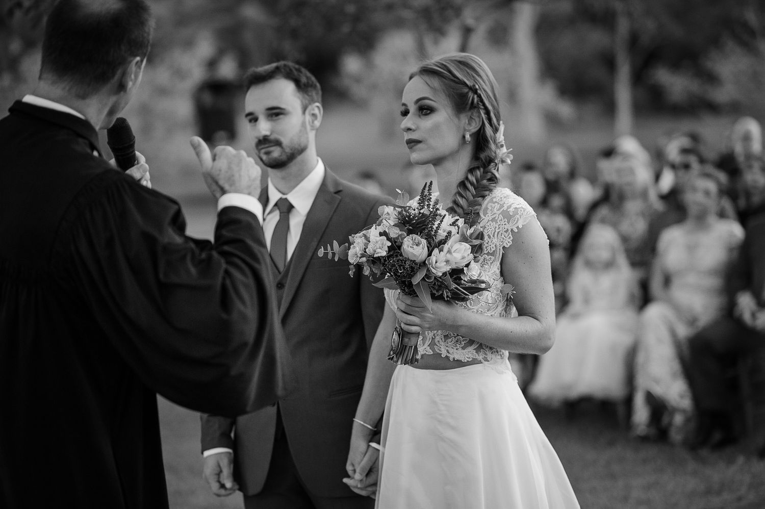 A black and white photo of a wedding ceremony being officiated in front of seated guests.