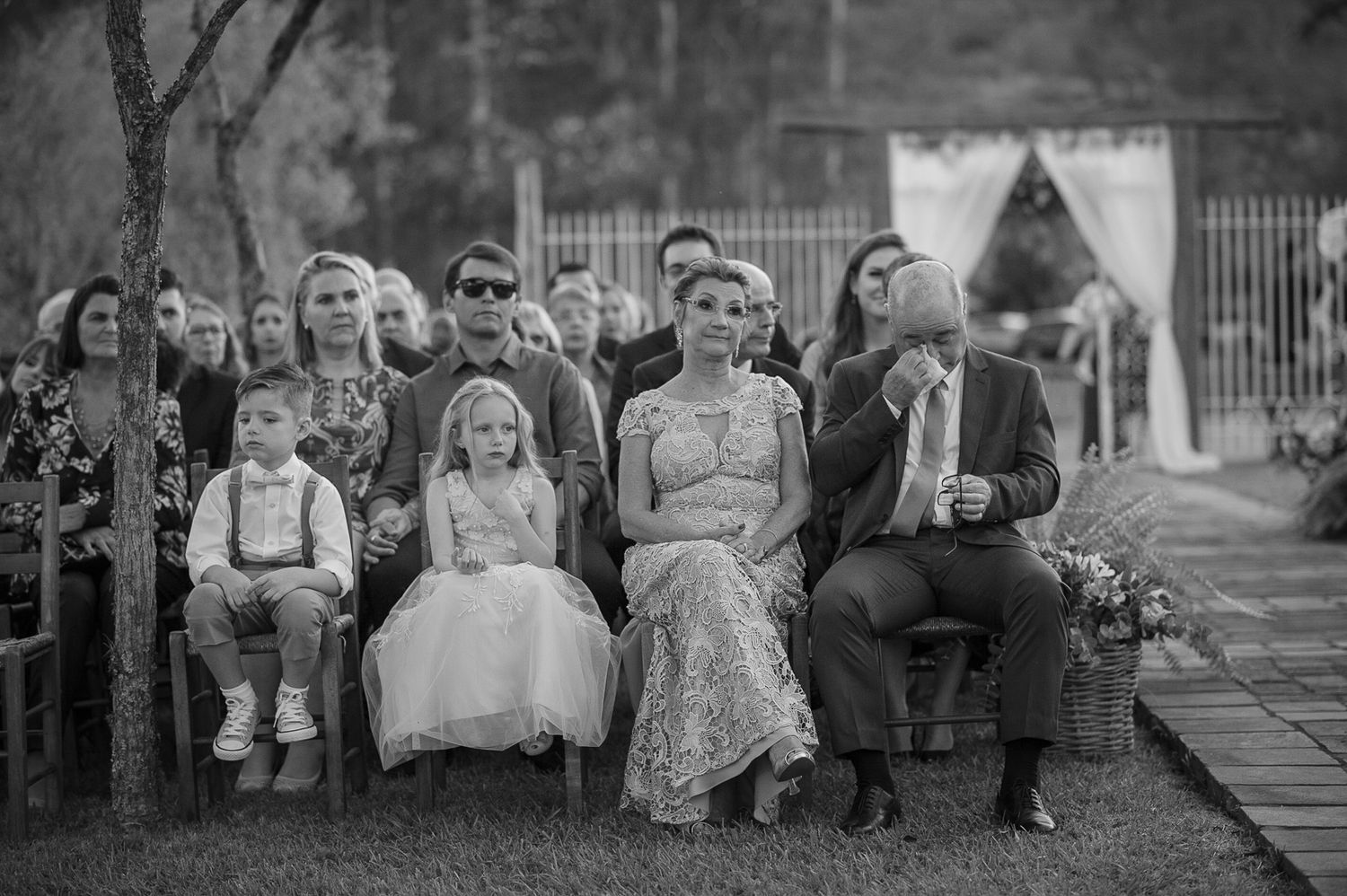 Wedding guests watching the ceremony from wooden chairs in a black and white photo.