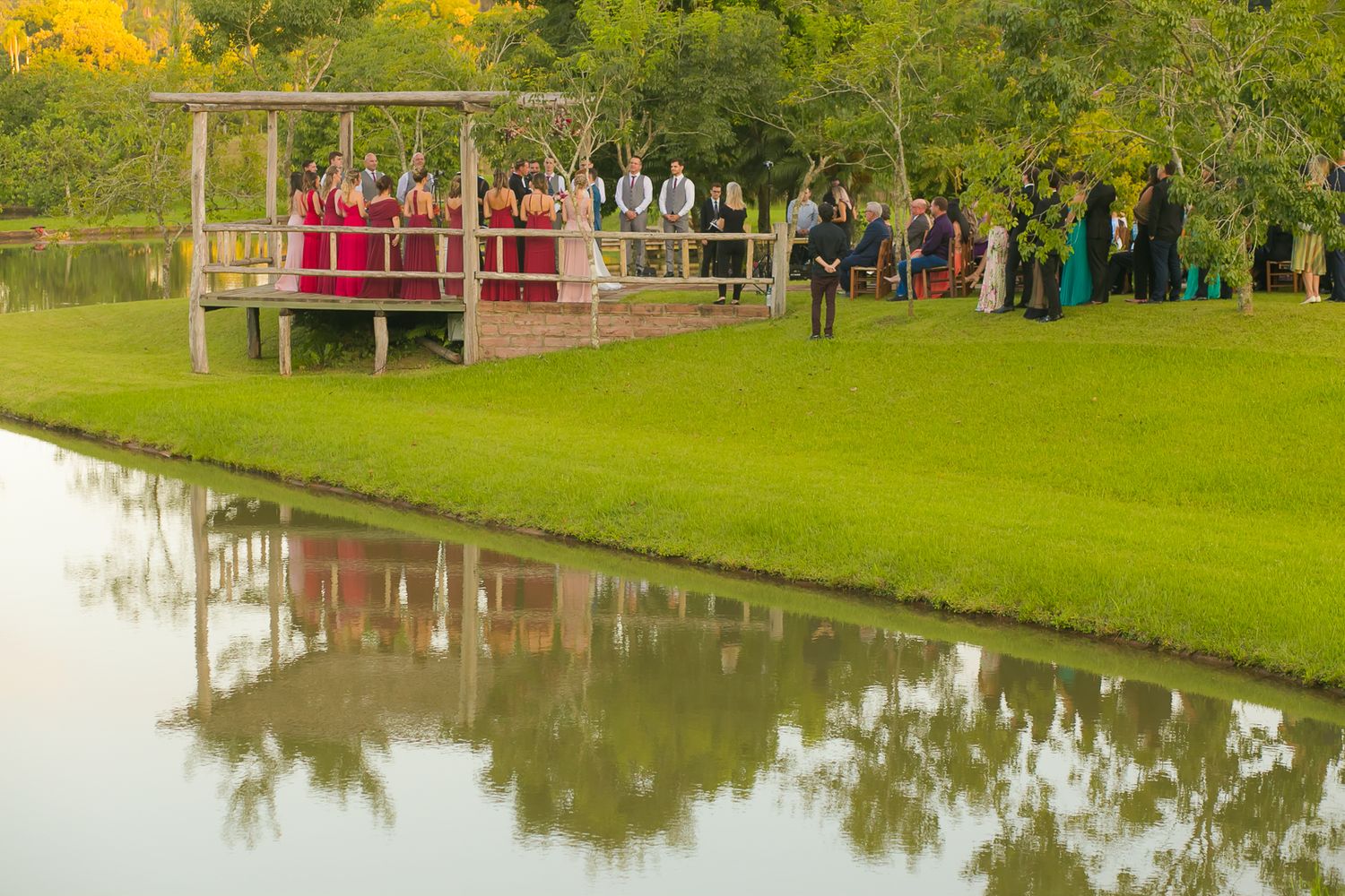 Wedding guests gathered on a wooden deck overlooking a pond during an outdoor ceremony.