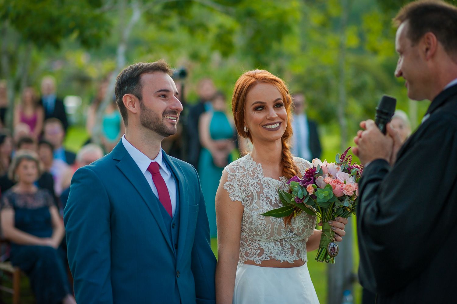 A joyful outdoor wedding ceremony with floral bouquet and natural greenery.