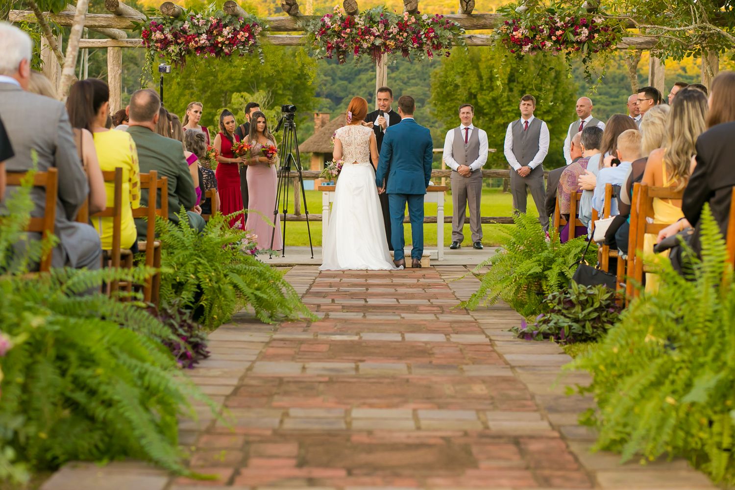 Garden wedding ceremony on a stone pathway with ferns and floral arches.
