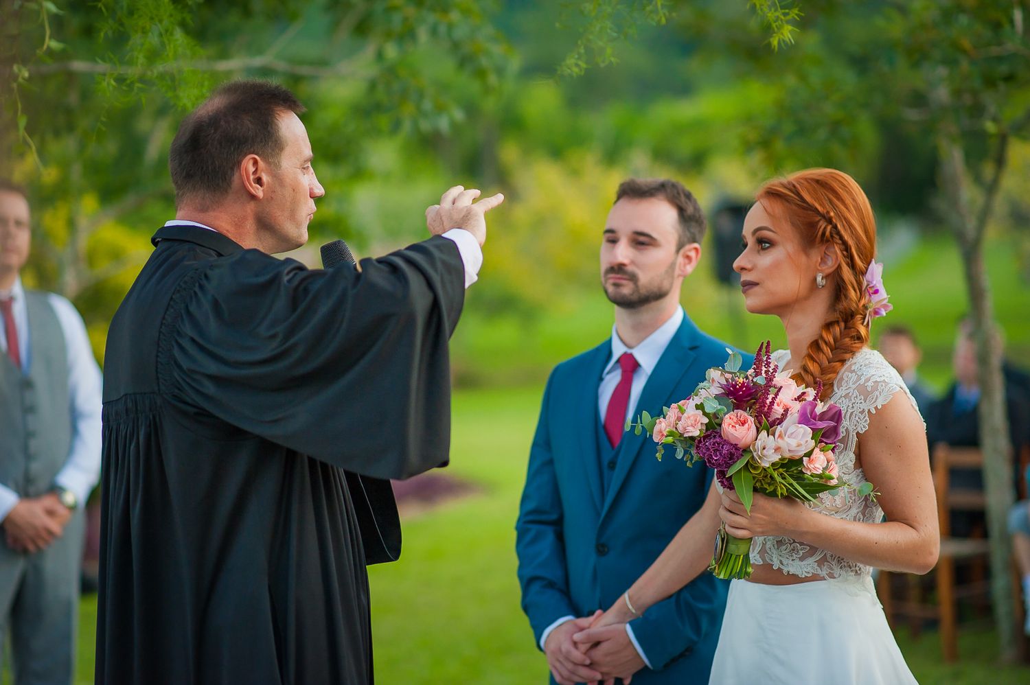 Outdoor wedding ceremony being conducted by an officiant in traditional robes.