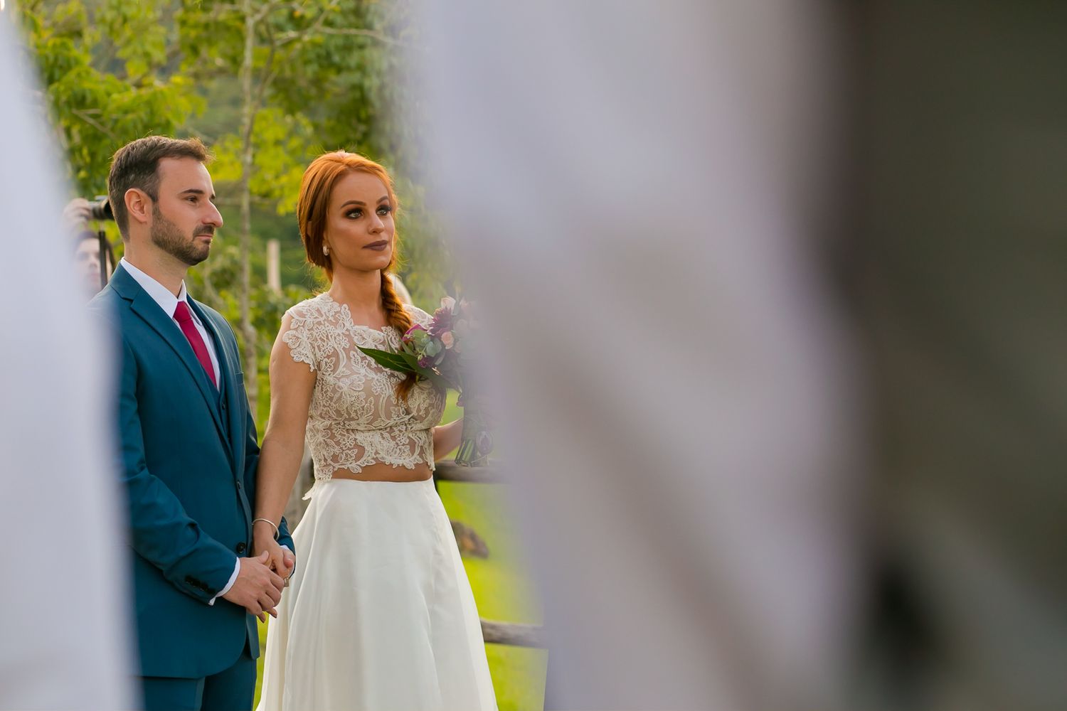 Intimate wedding ceremony moment captured through foreground elements in natural setting.
