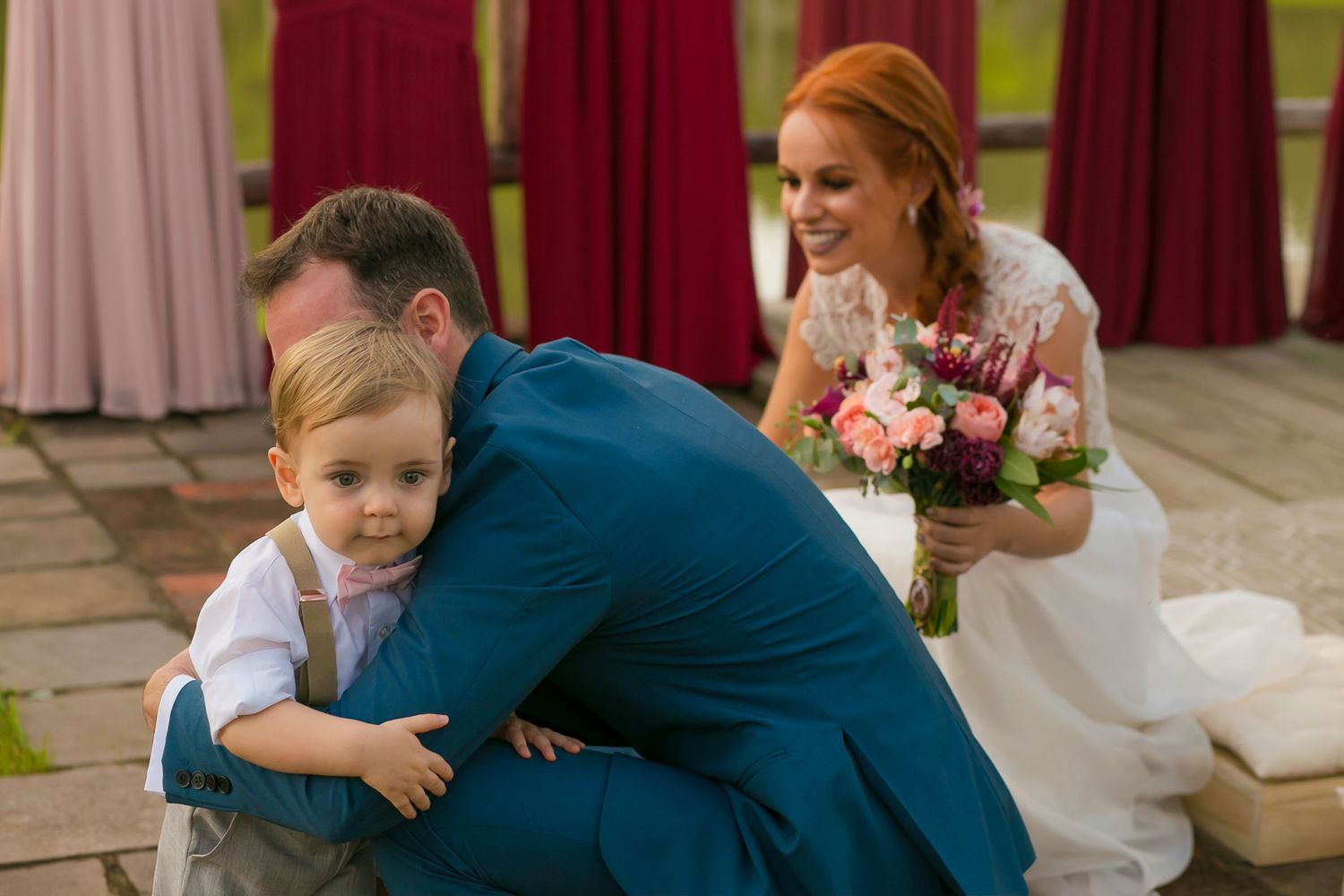 Sweet moment between child and adults during wedding celebration with pink floral bouquet.