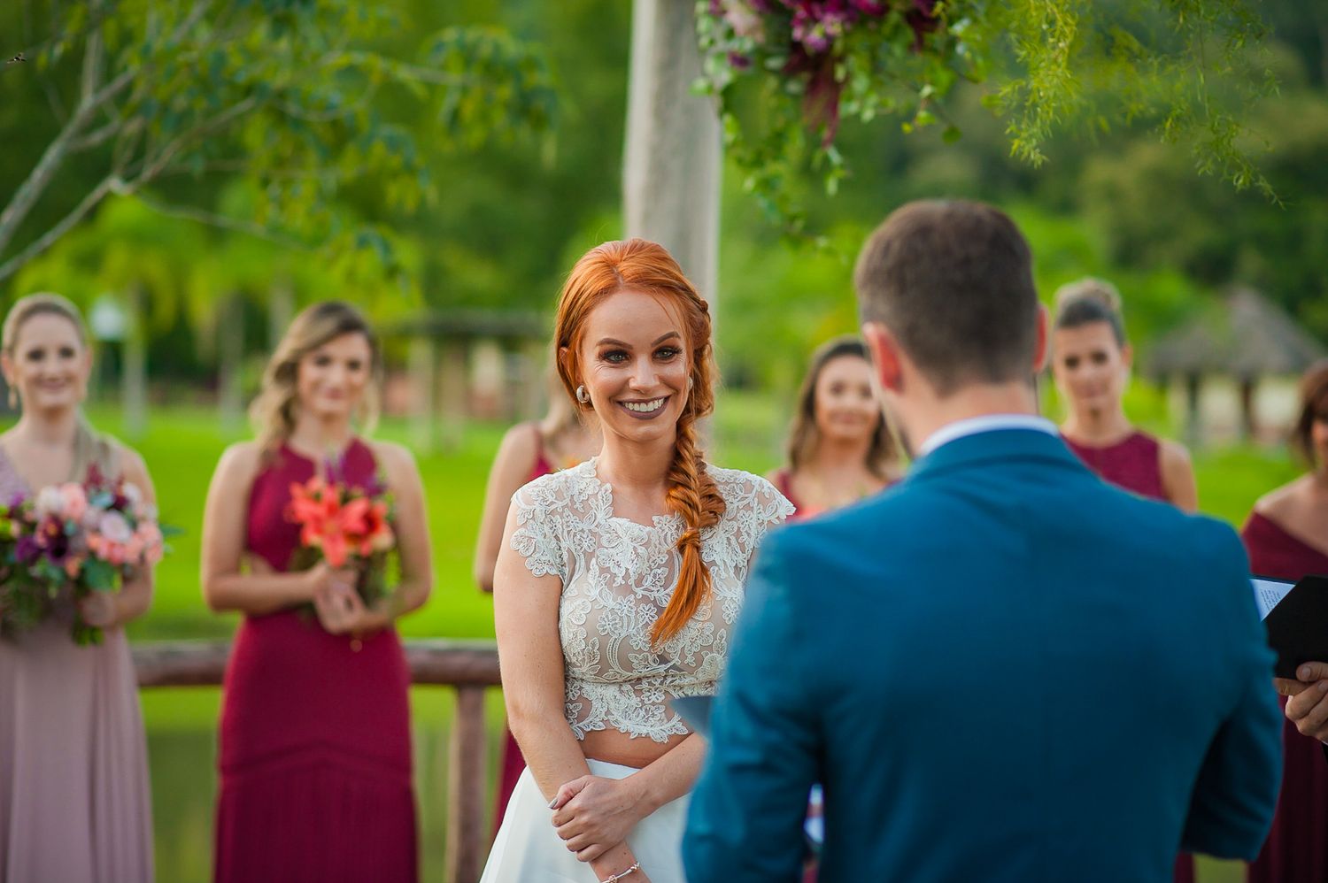 Outdoor wedding ceremony with bridesmaids in burgundy dresses in background.