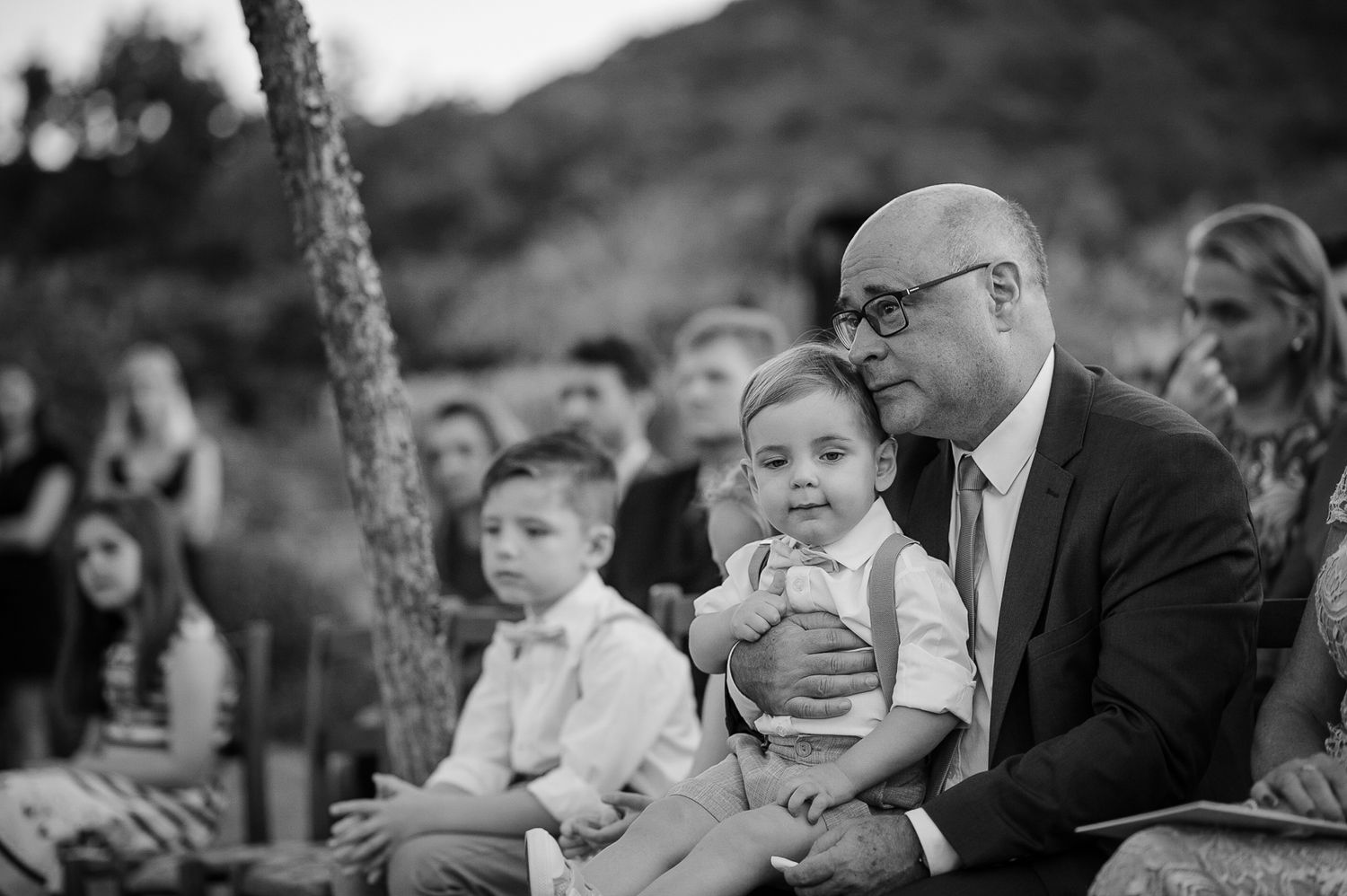 Black and white photo of wedding guests watching ceremony from outdoor seating.