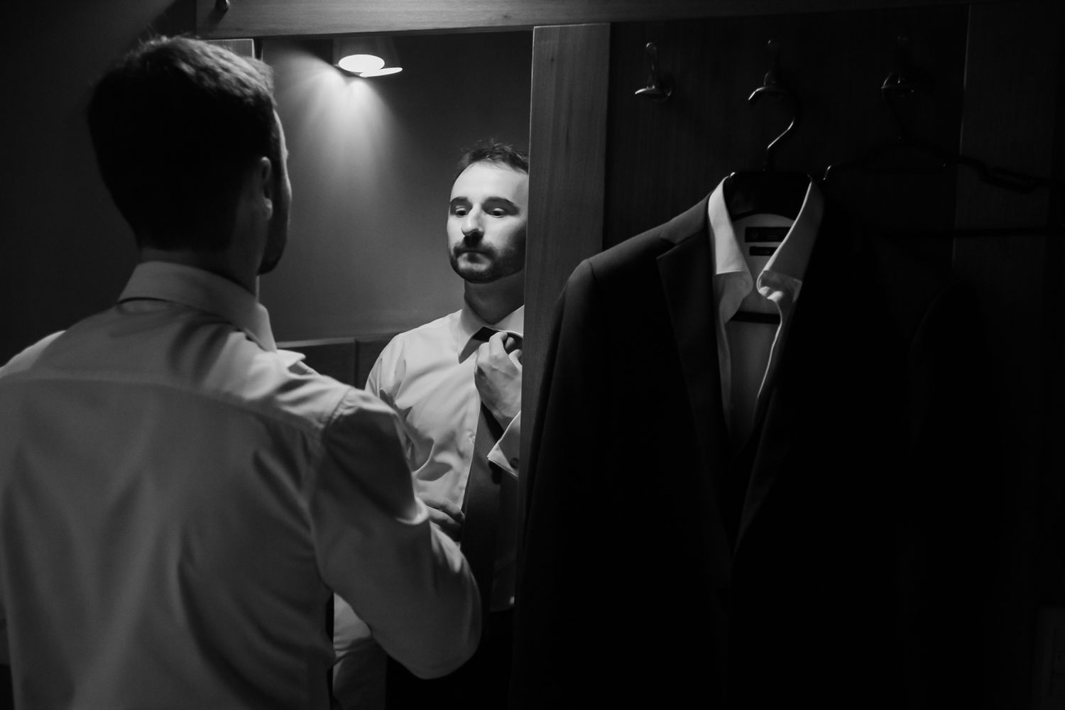Two people discussing clothing choices near a rack of formal wear in dramatic lighting.