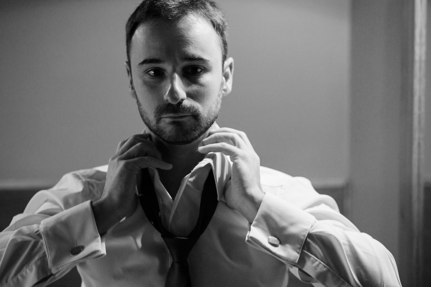 Person adjusting a tie while getting dressed in formal attire, captured in black and white.
