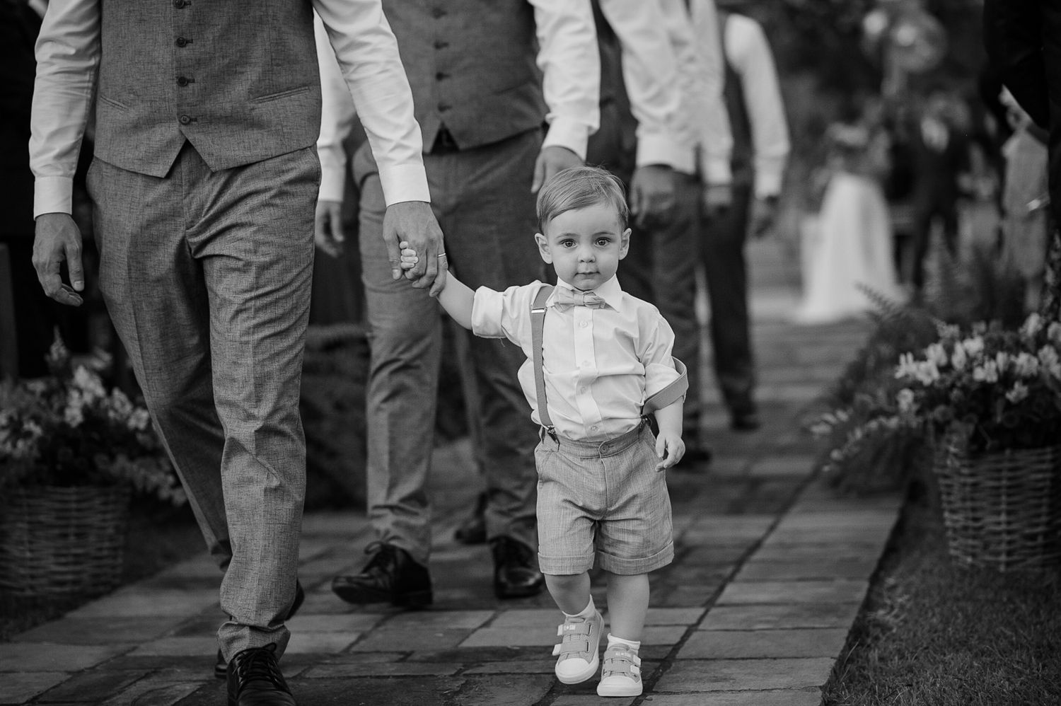 A black and white photo of a young child walking down an aisle holding hands with adults.