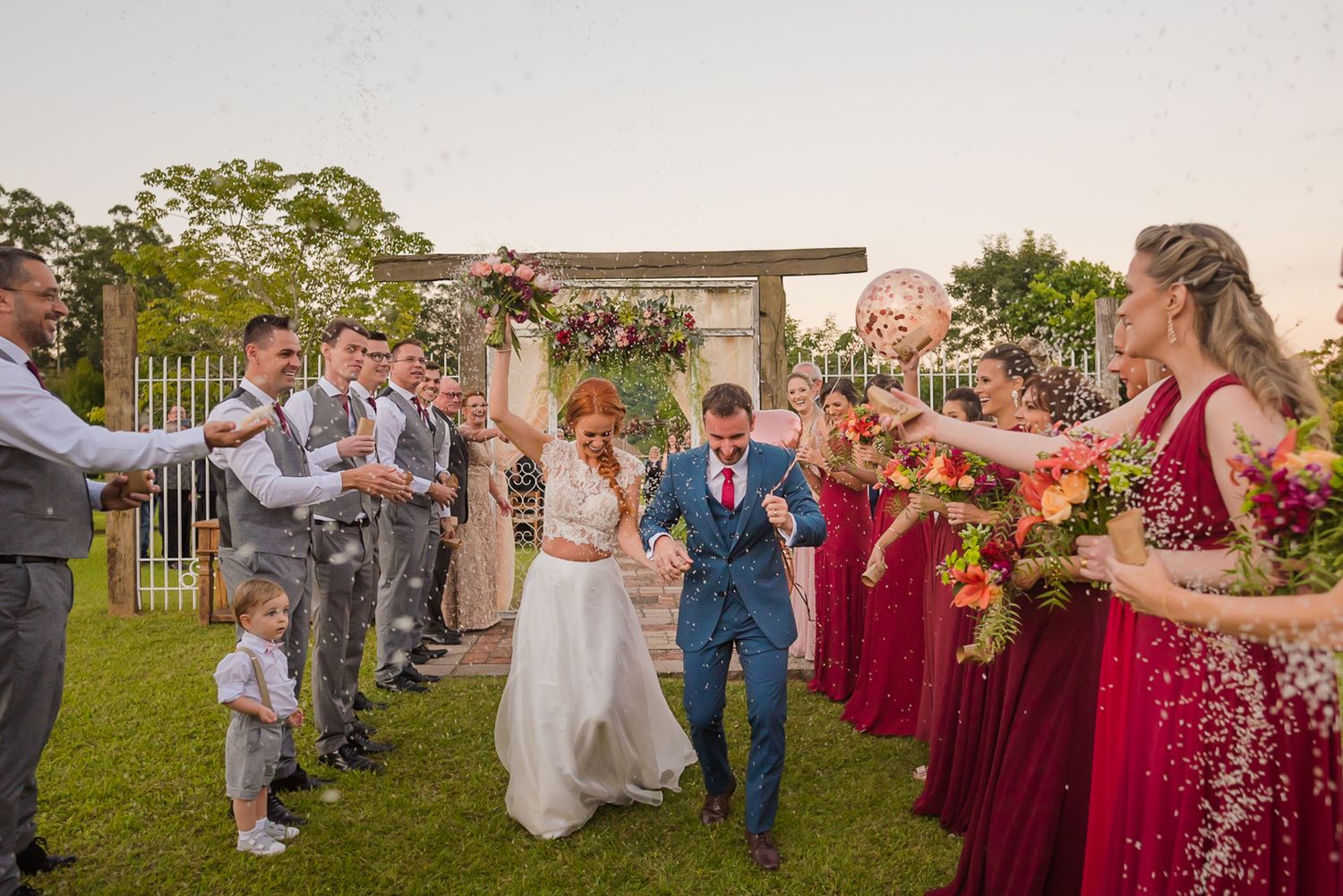 Wedding party throws confetti at outdoor ceremony while guests line pathway.