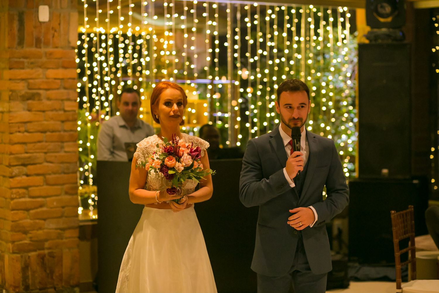 A wedding couple stands against a backdrop of twinkling fairy lights during their reception celebration.