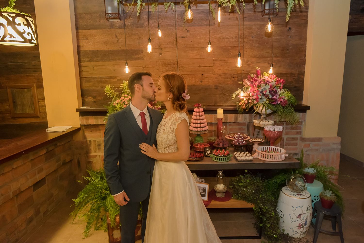 A romantic moment at a wedding dessert table decorated with flowers and hanging lights.