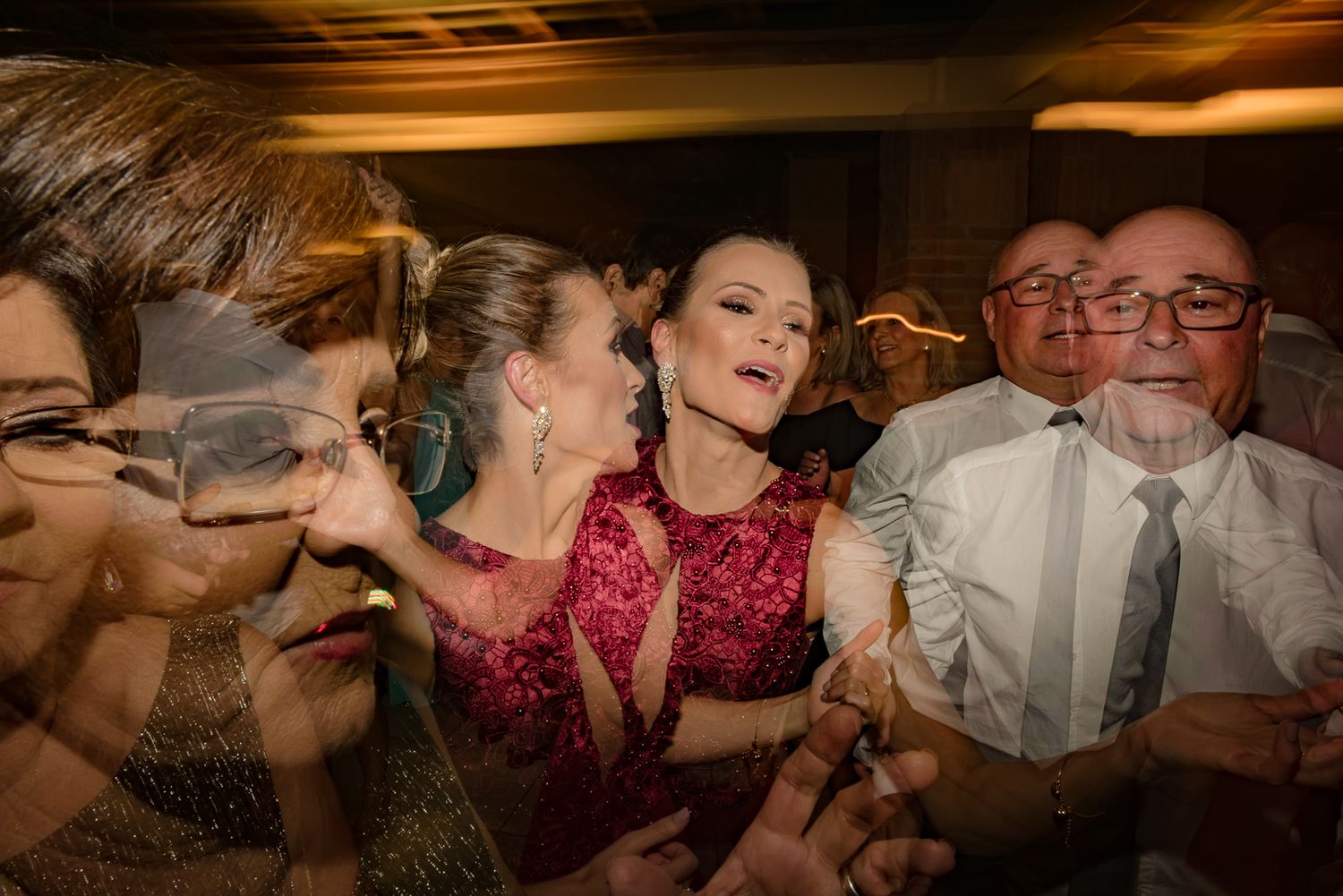 Wedding reception party guests singing and laughing during an animated moment at an indoor celebration.