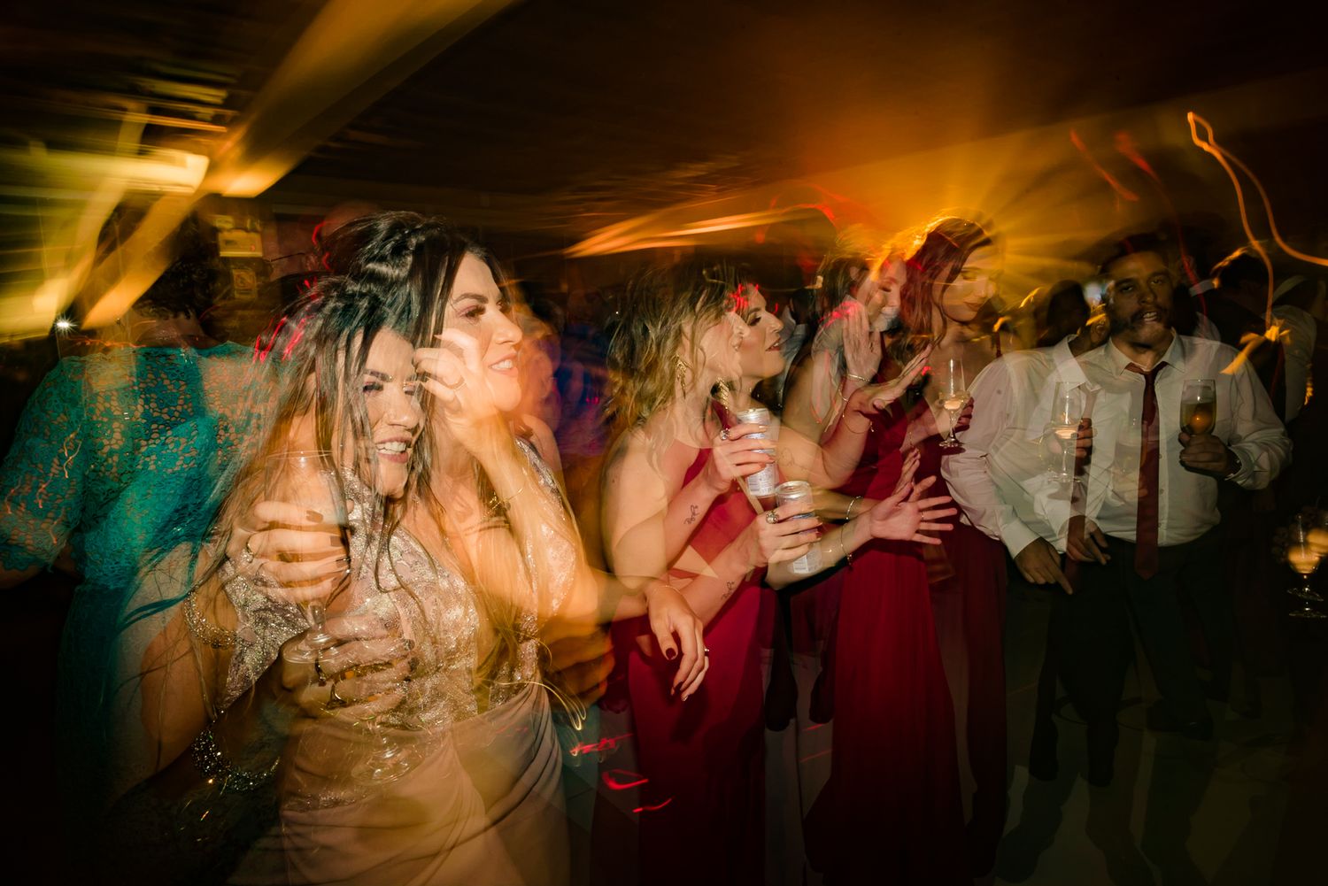 Wedding guests dancing enthusiastically under warm lighting at a lively reception party.