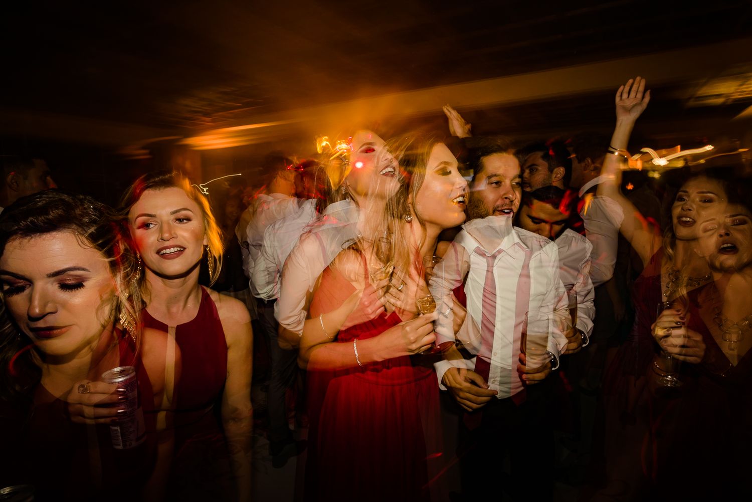 Energetic crowd dancing and celebrating at a dimly lit wedding reception.
