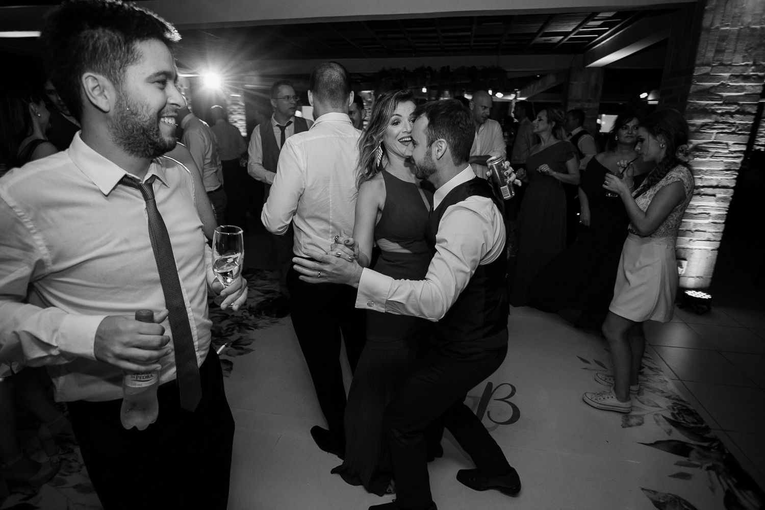 Black and white photo of wedding guests mingling and dancing at an indoor reception.