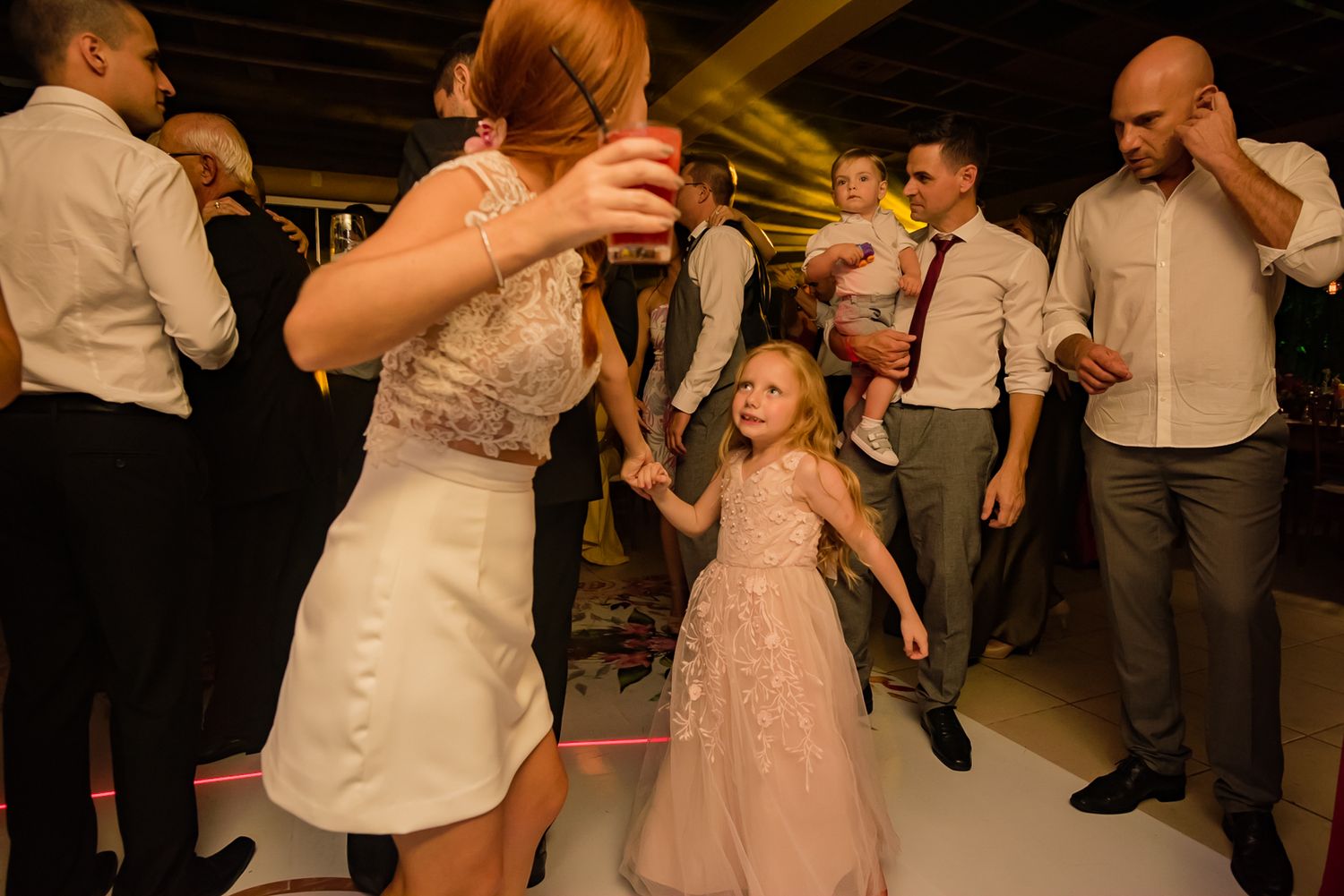 Young guest in a flowing dress dancing joyfully with adults at a wedding reception.