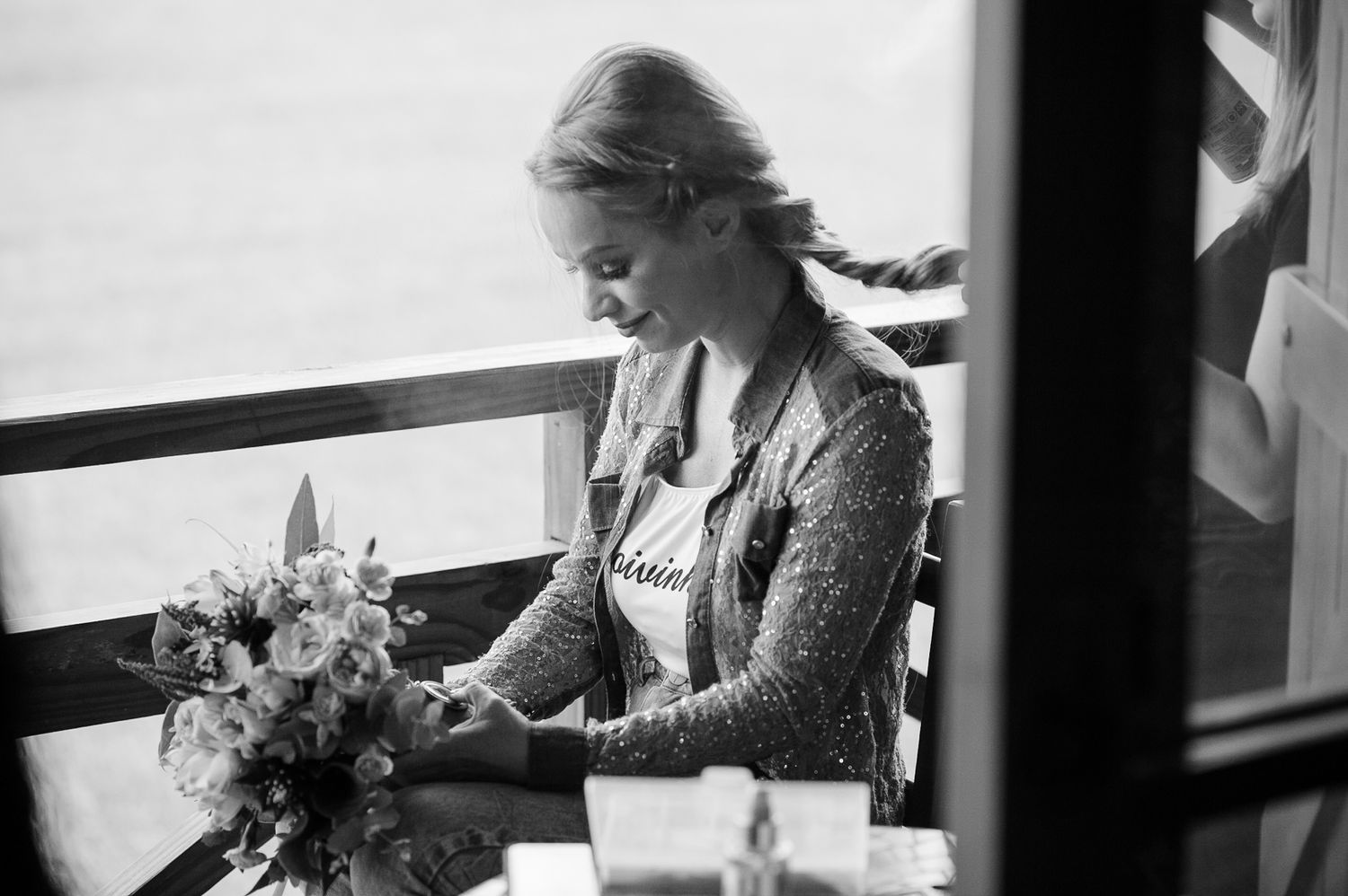 Person in elegant dress arranging flowers by a window in black and white photography.