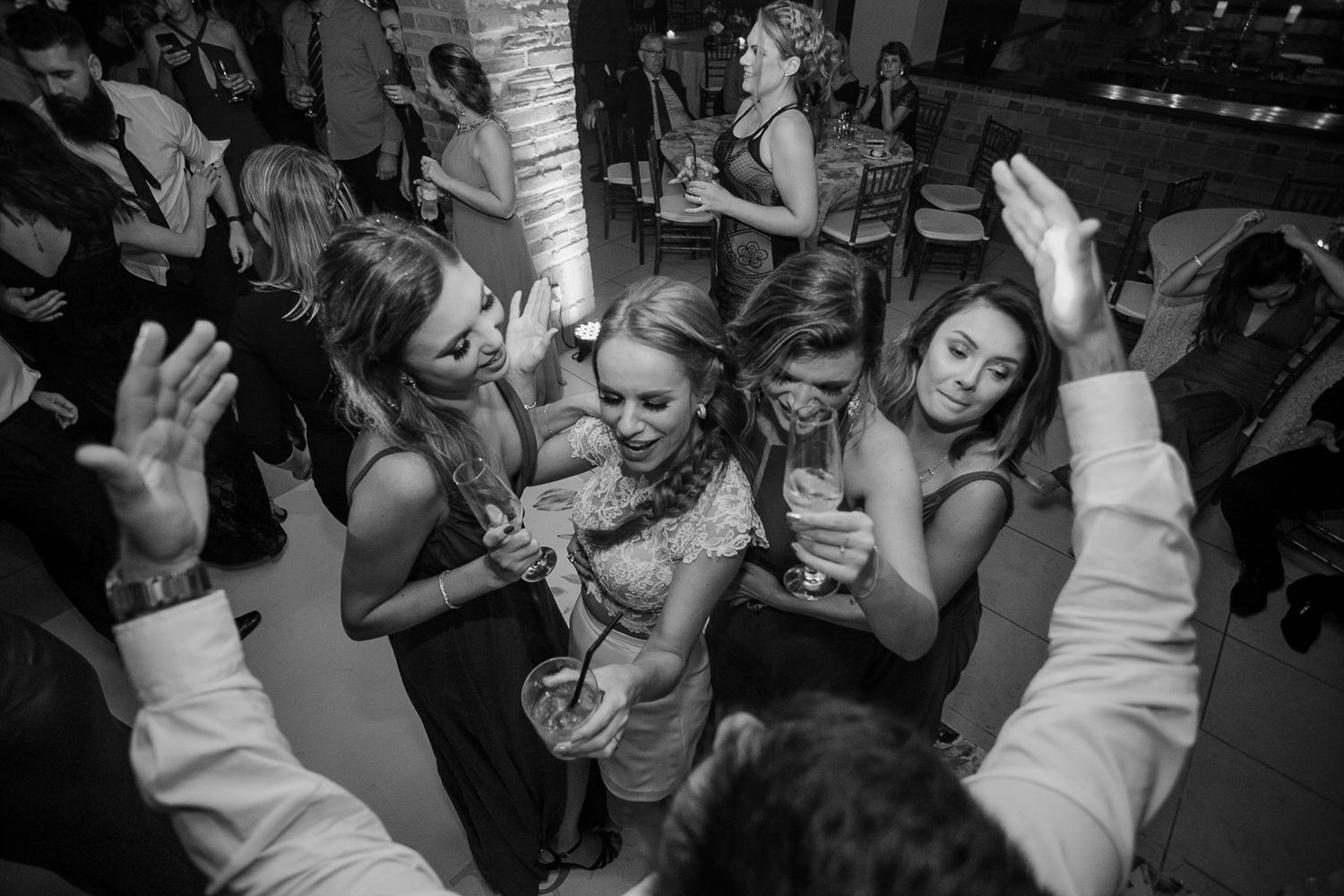 Black and white photo of wedding guests dancing and celebrating with raised hands on the dance floor.