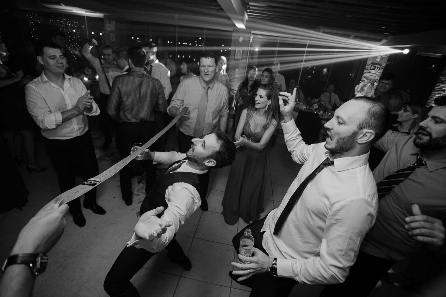 Wedding guests dancing energetically under dramatic lighting at reception.