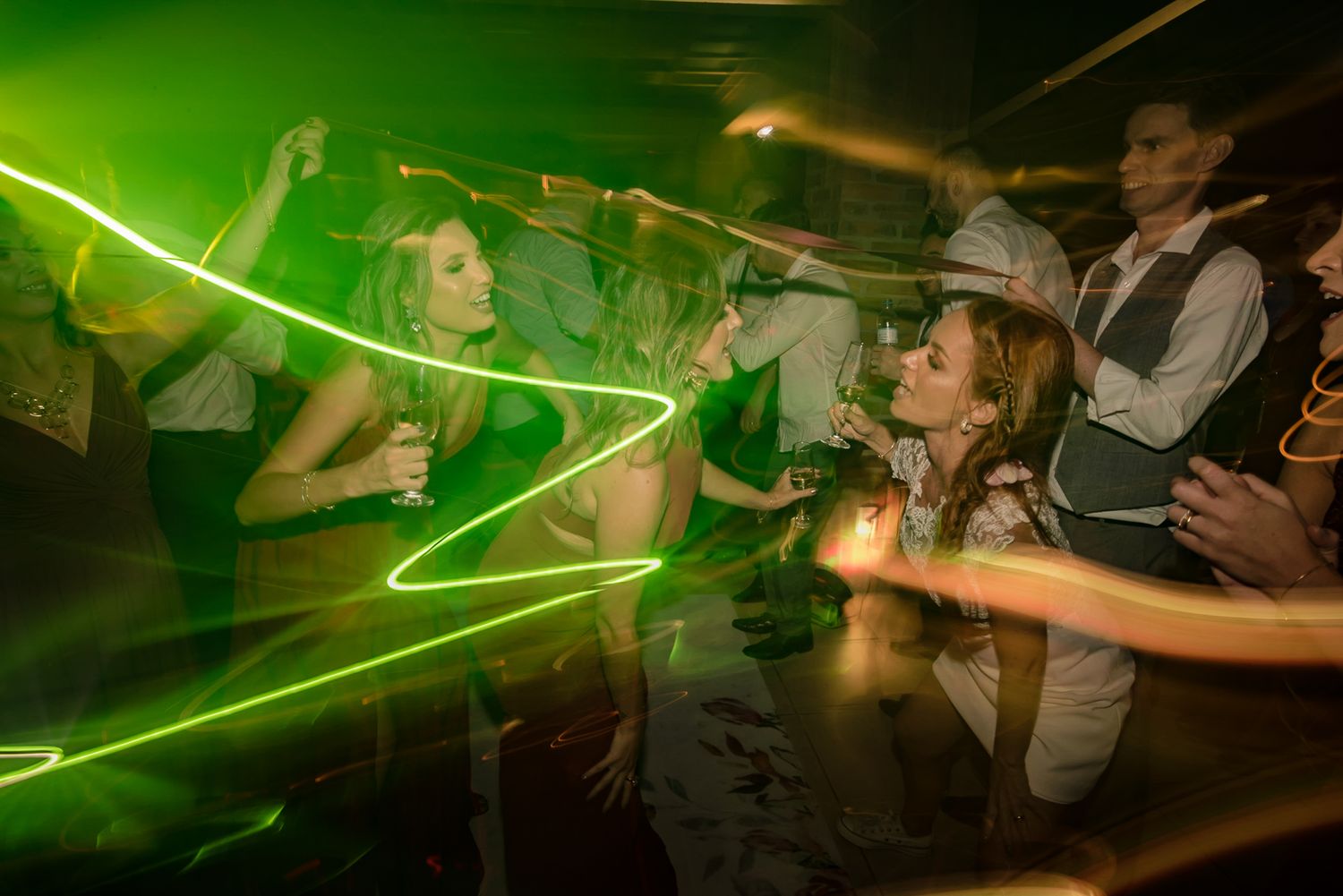 Green laser lights create dynamic patterns across dancing wedding guests.