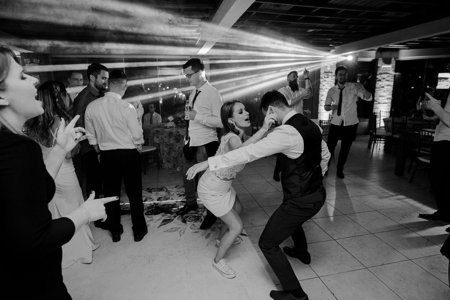 Black and white photo of people dancing energetically at a wedding reception.