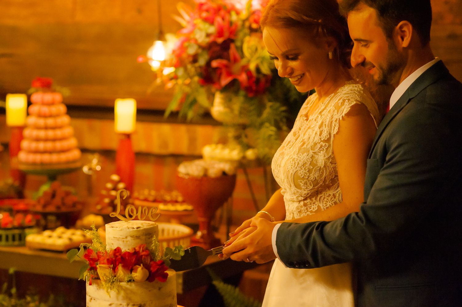 A couple cutting their wedding cake surrounded by candlelight and floral arrangements.