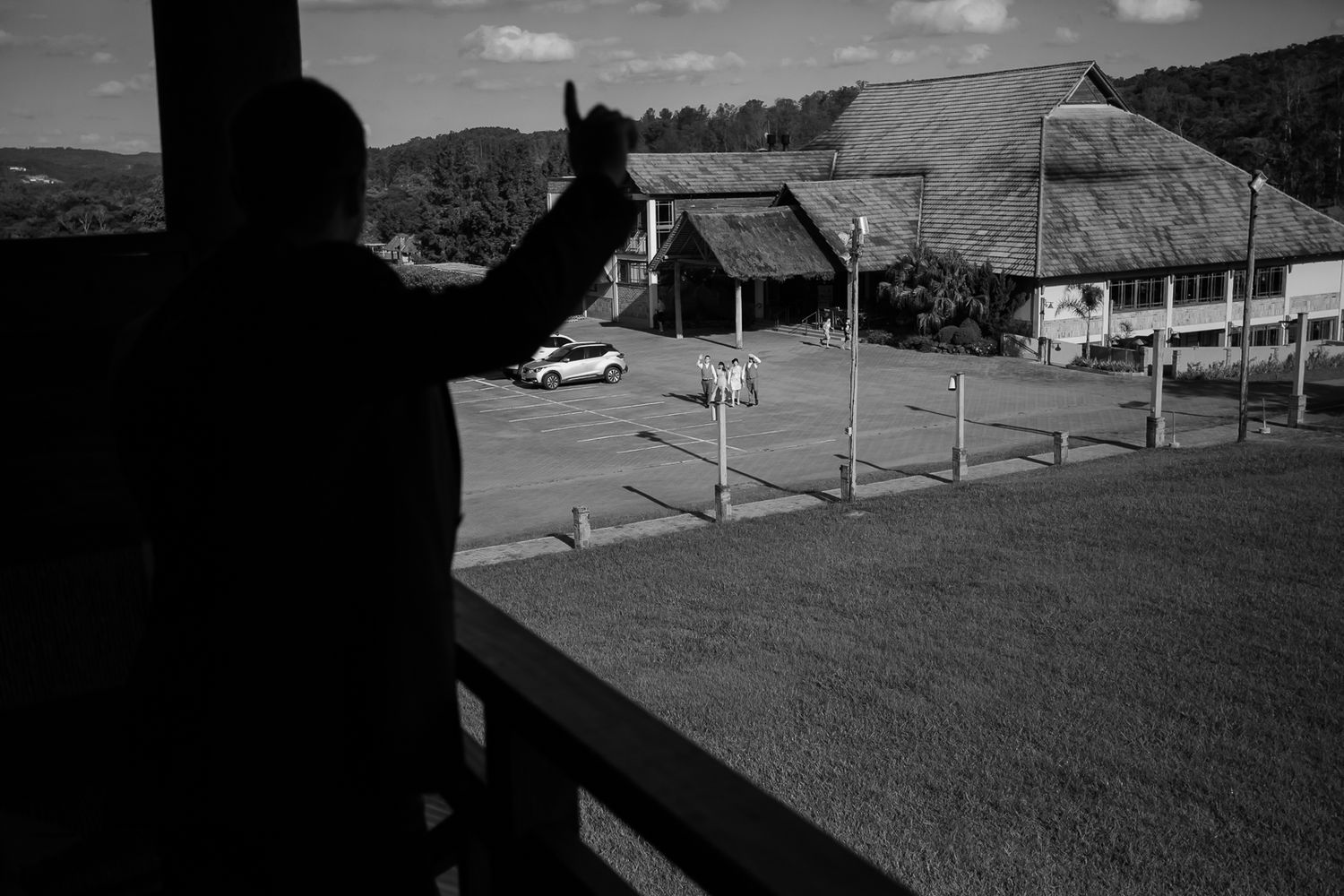 Silhouetted figure overlooking rural buildings and parking area from elevated position.
