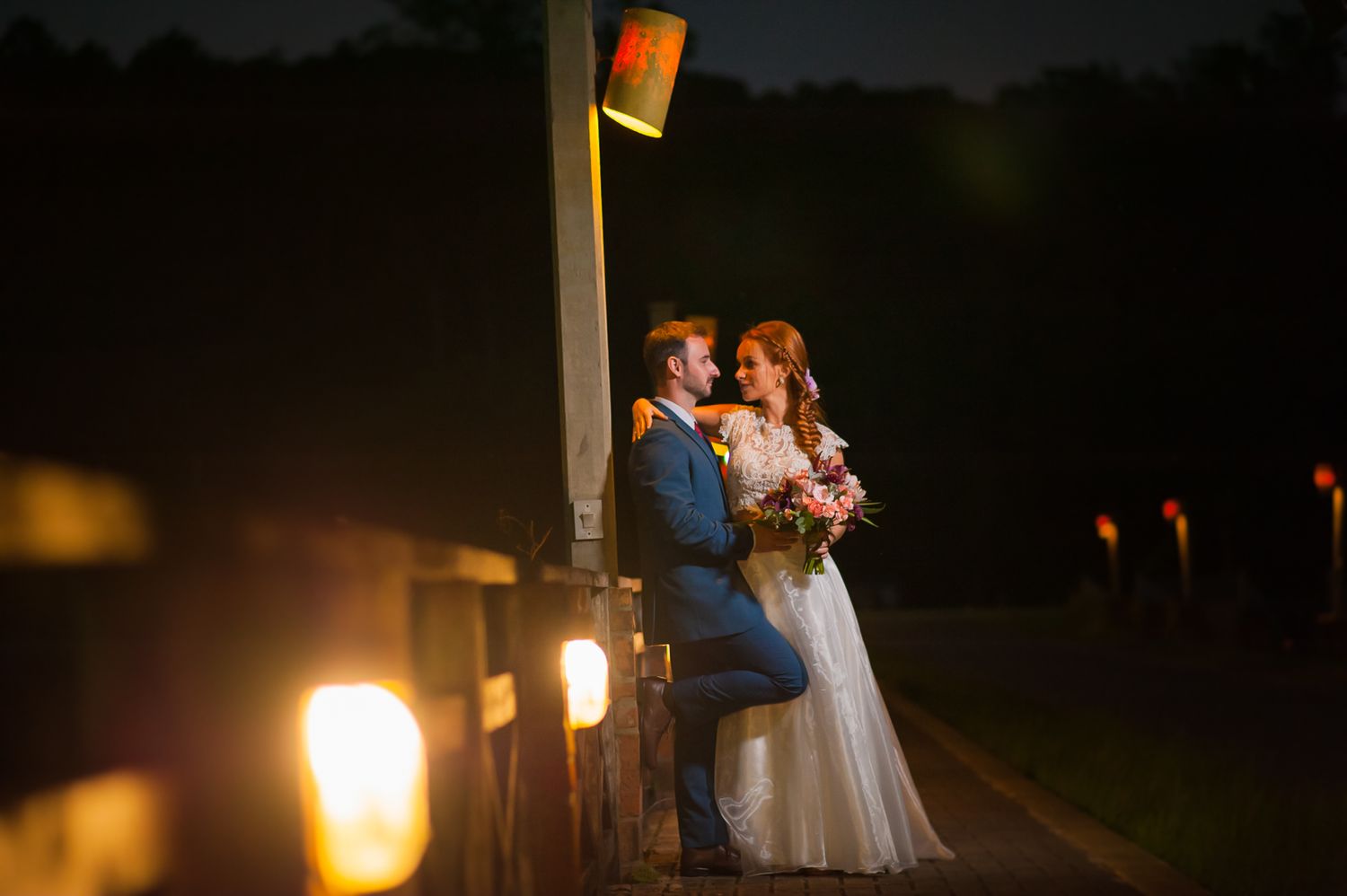 A romantic evening portrait illuminated by warm glowing lights on a wooden post.