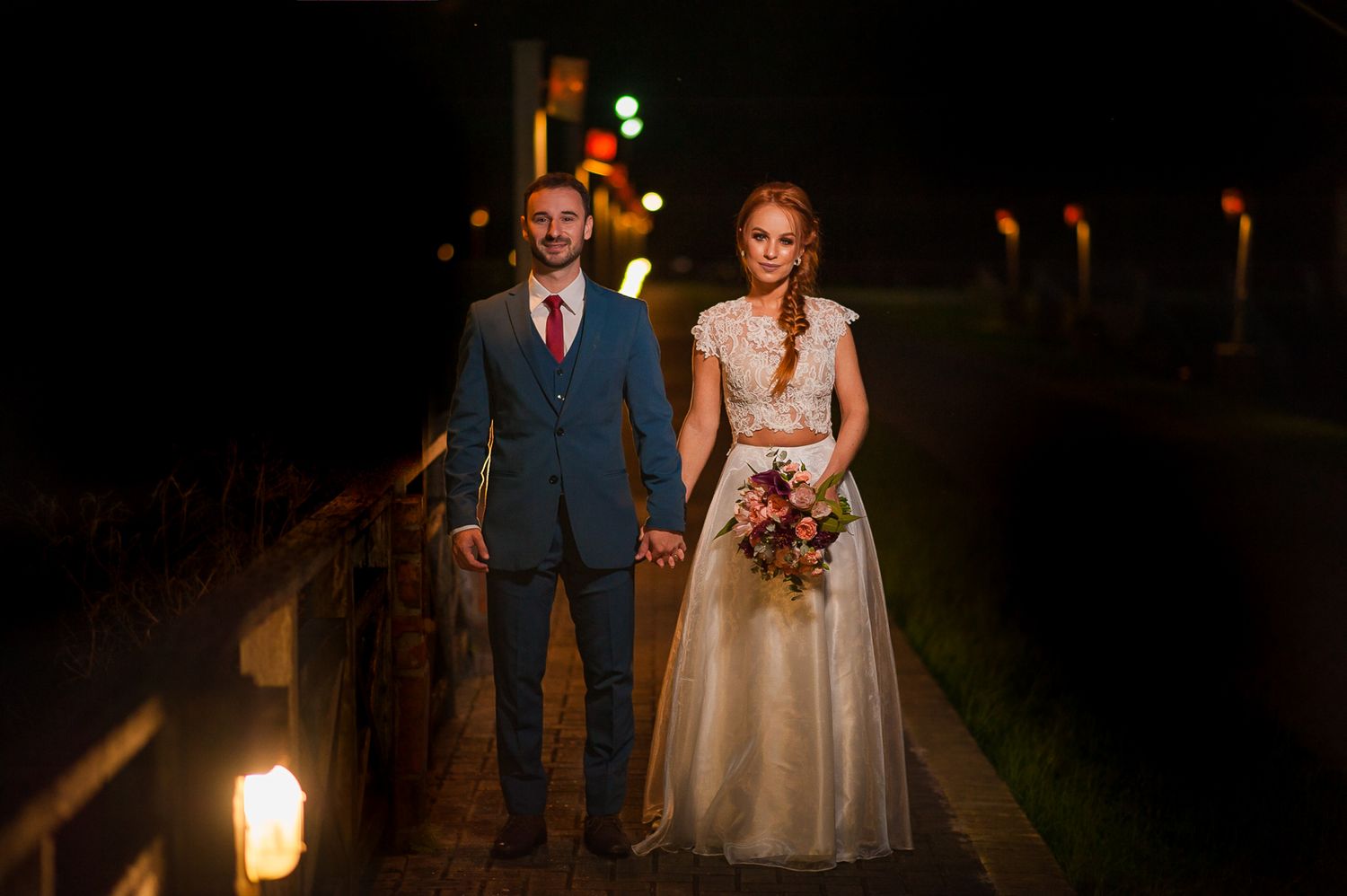 A couple standing together on an illuminated walkway at night.