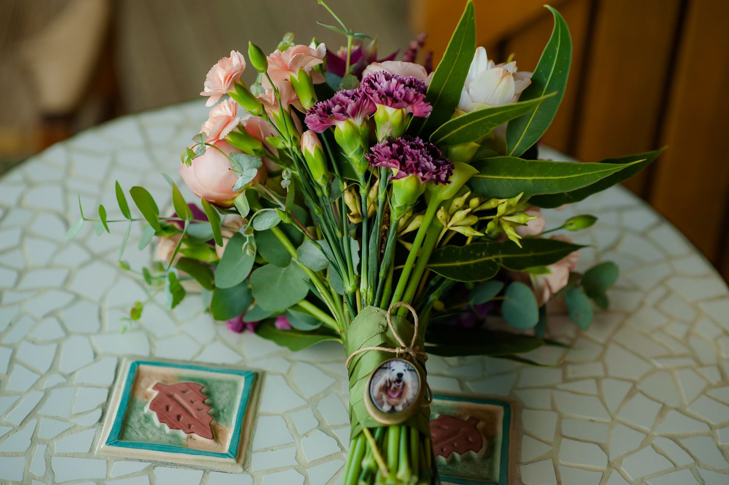 Fresh flower arrangement with pink and purple blooms in vase with small frames on patterned tablecloth.