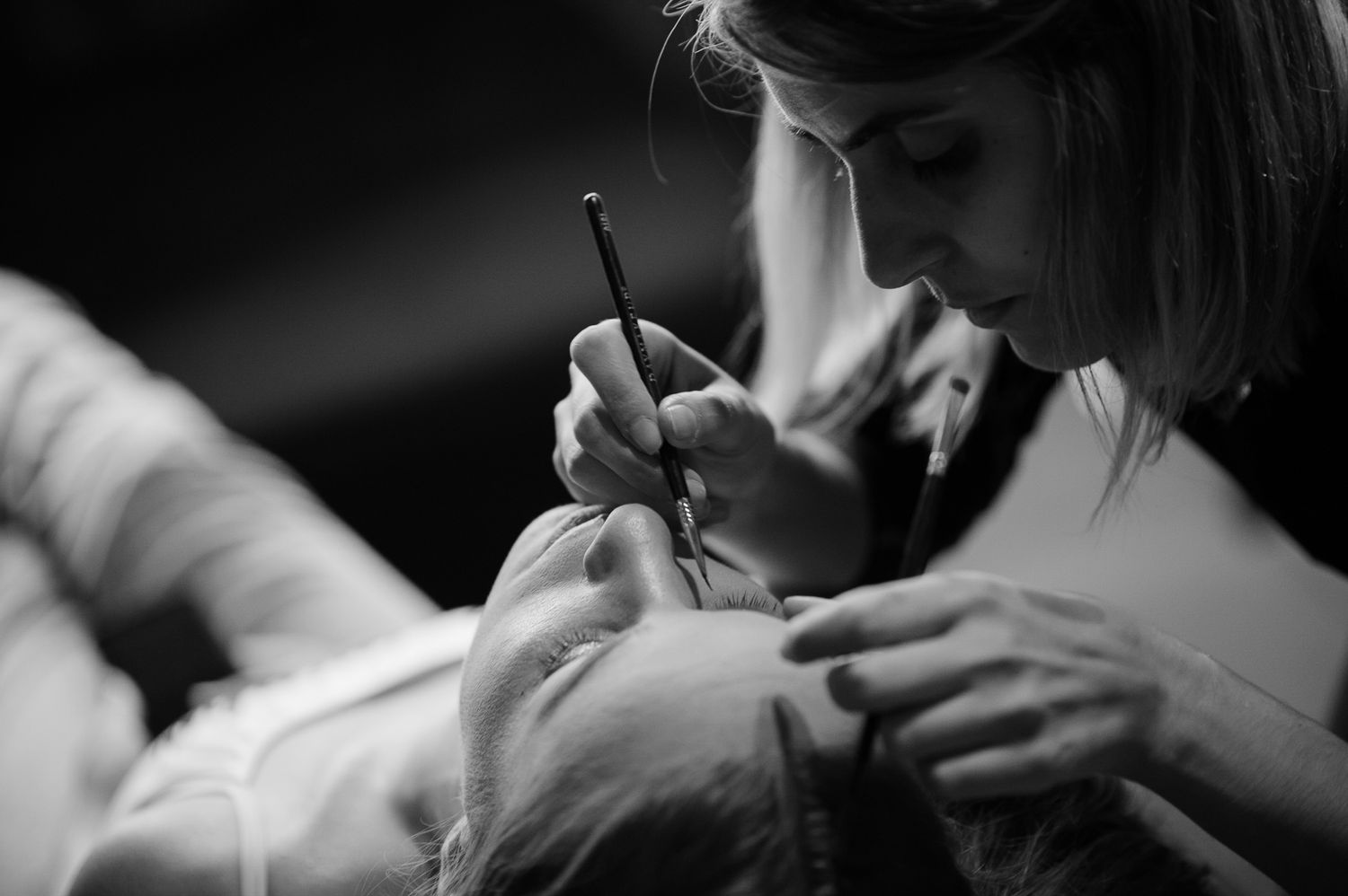 A close-up black and white image showing a delicate makeup application process.