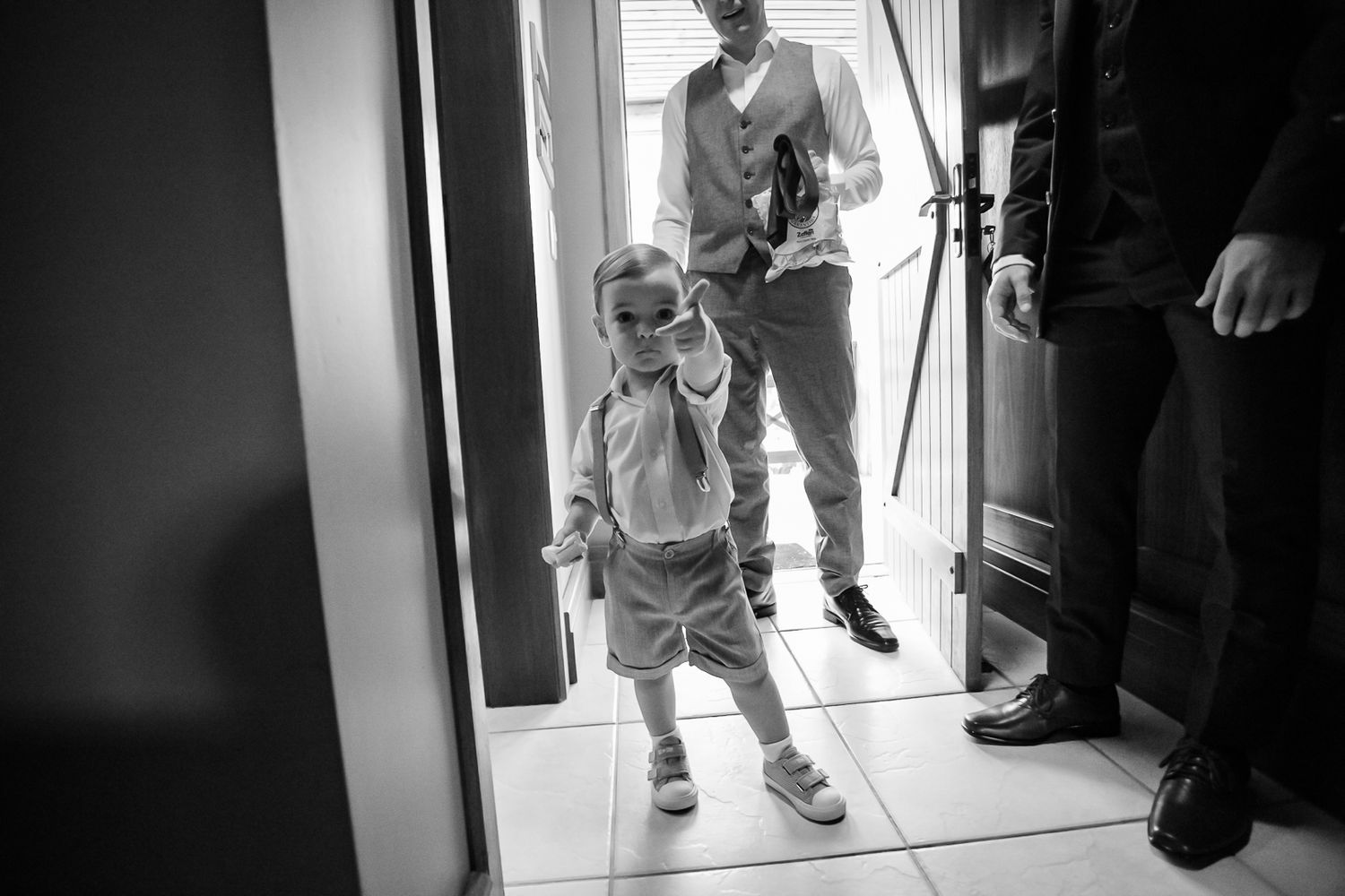 A black and white image captures a small child in formal wear stepping through a doorway.