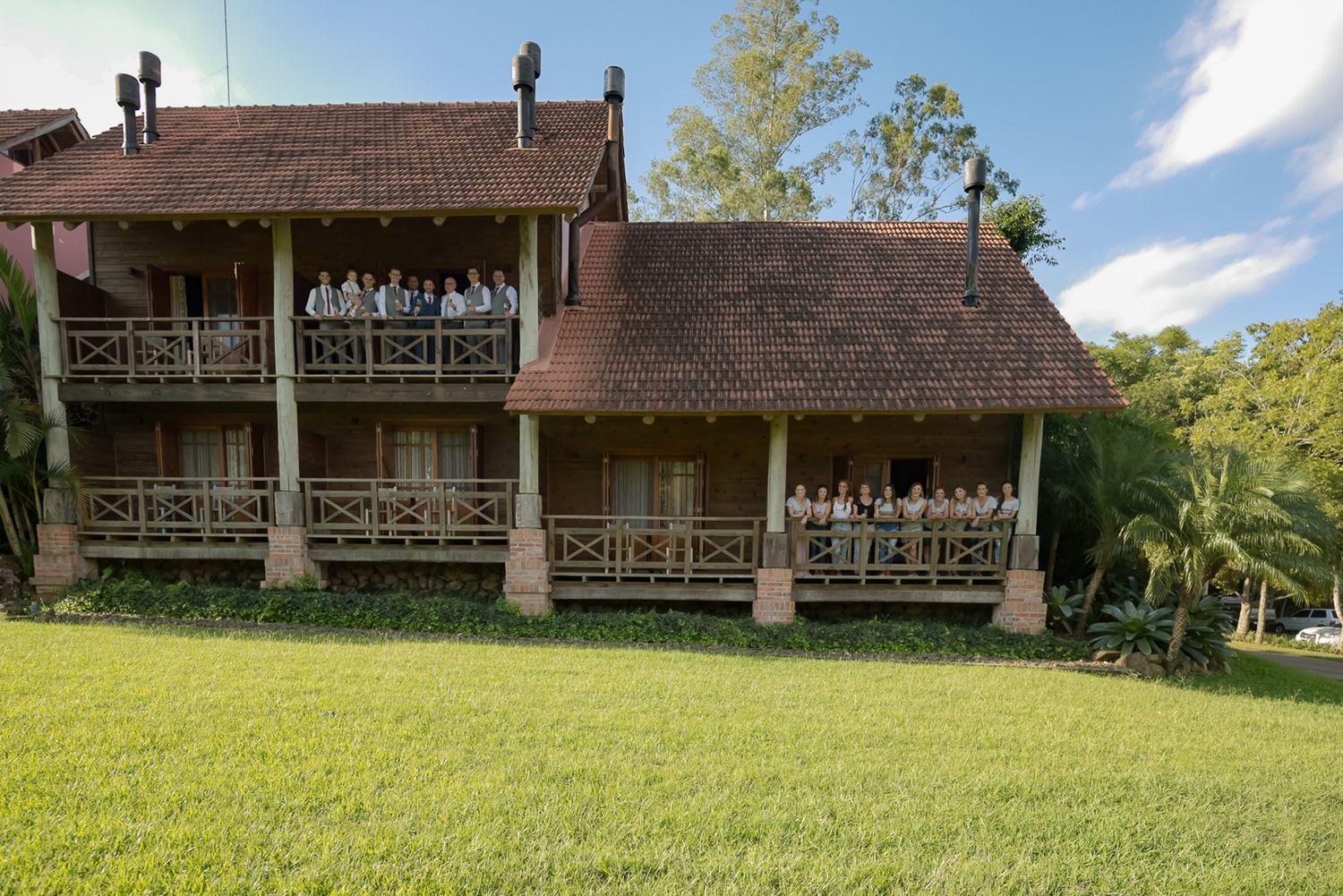 A rustic wooden lodge with multiple balconies sits nestled among trees on a sunny day.